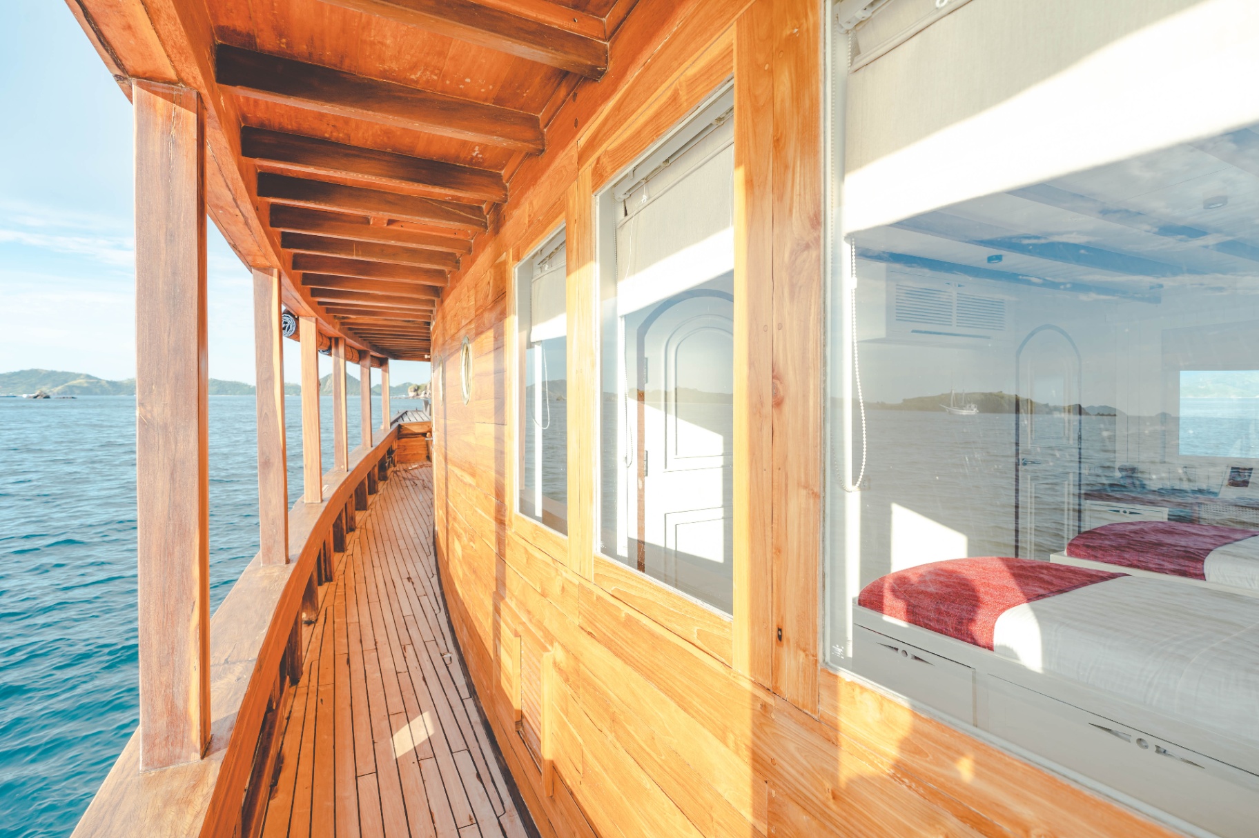 Mischief teak side deck at golden hour with cabin windows revealing a red-throw bed inside