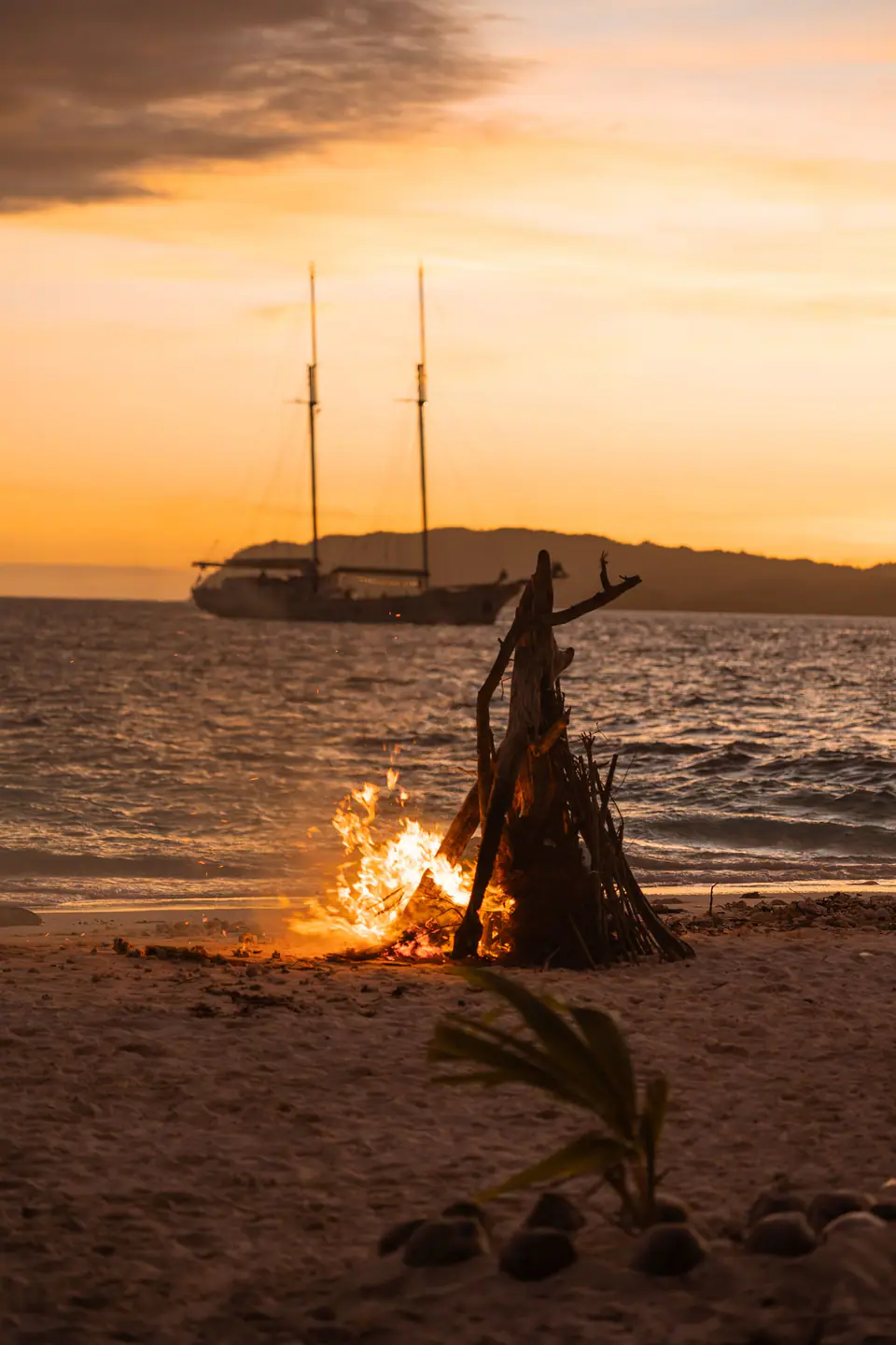 Beach bonfire at sunset with Mutiara Laut silhouetted on the horizon