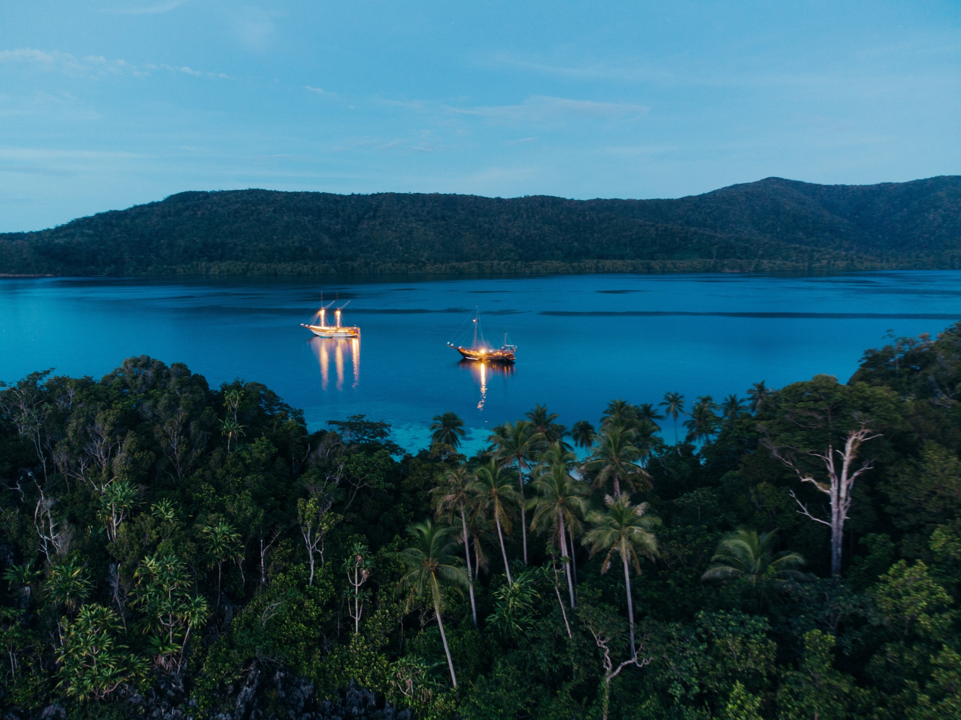 Senja anchored with lights reflecting on still water at blue hour in Raja Ampat