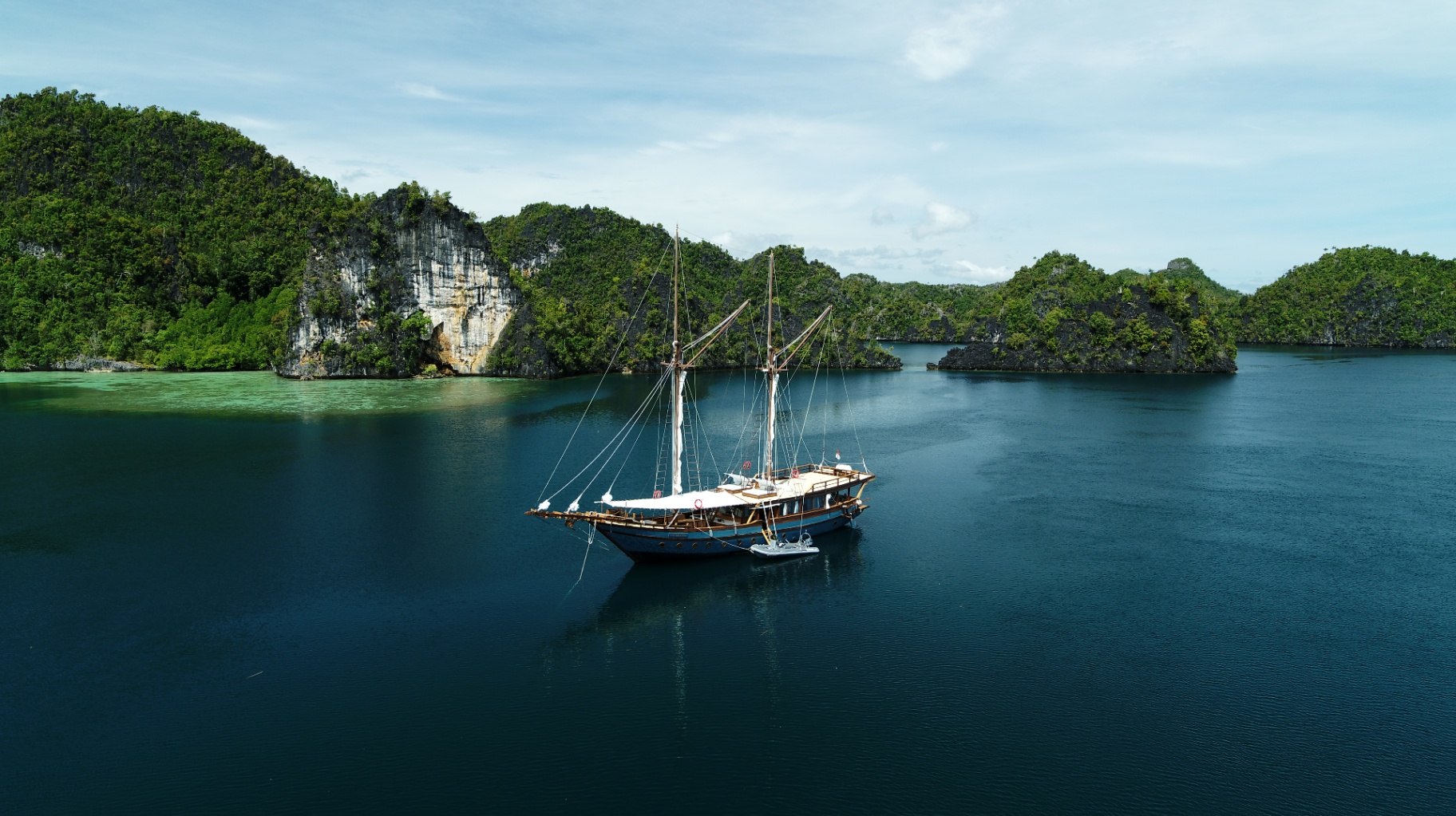 Drone view of Dewata anchored in deep blue water surrounded by karst islands