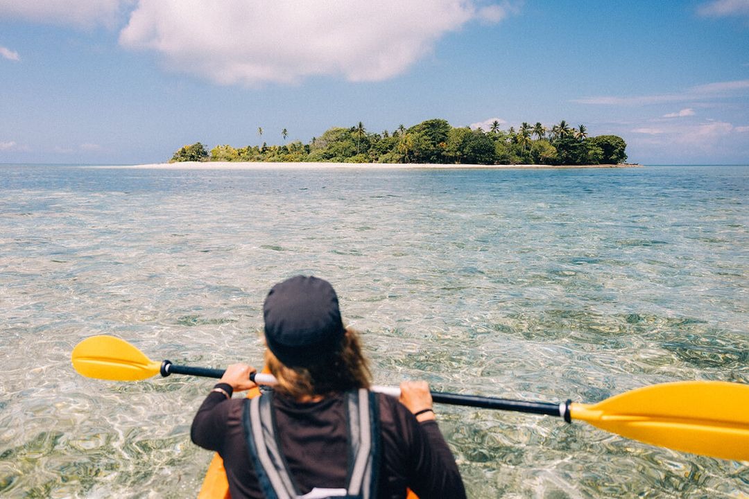Guest kayaking toward a small palm-fringed island on turquoise water