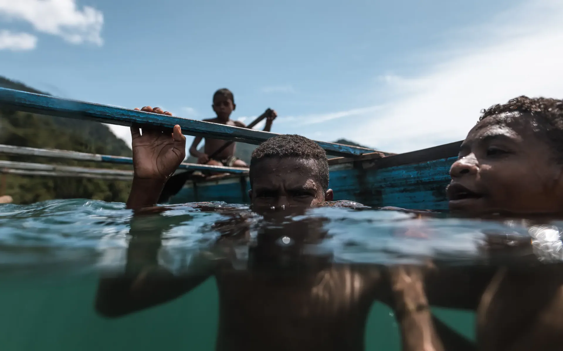 Local Papuan children in a wooden canoe meeting swimmers in Raja Ampat