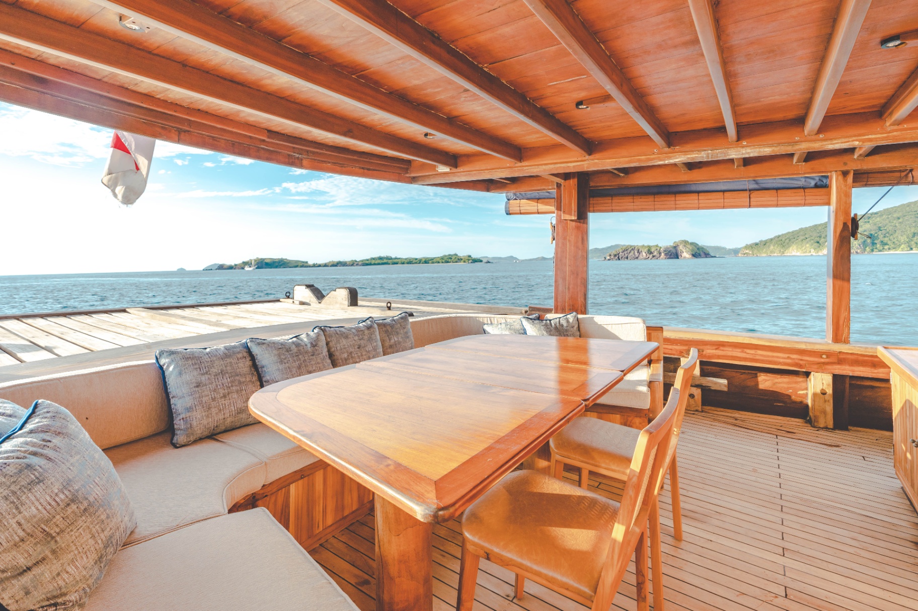 Mischief covered outdoor dining nook with cushioned banquette, wooden table and 180° ocean views