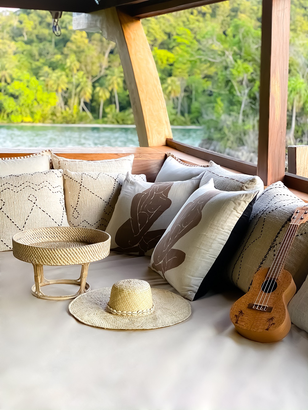 Shaded lounge corner on Senja with woven cushions, straw hat, ukulele and jungle views