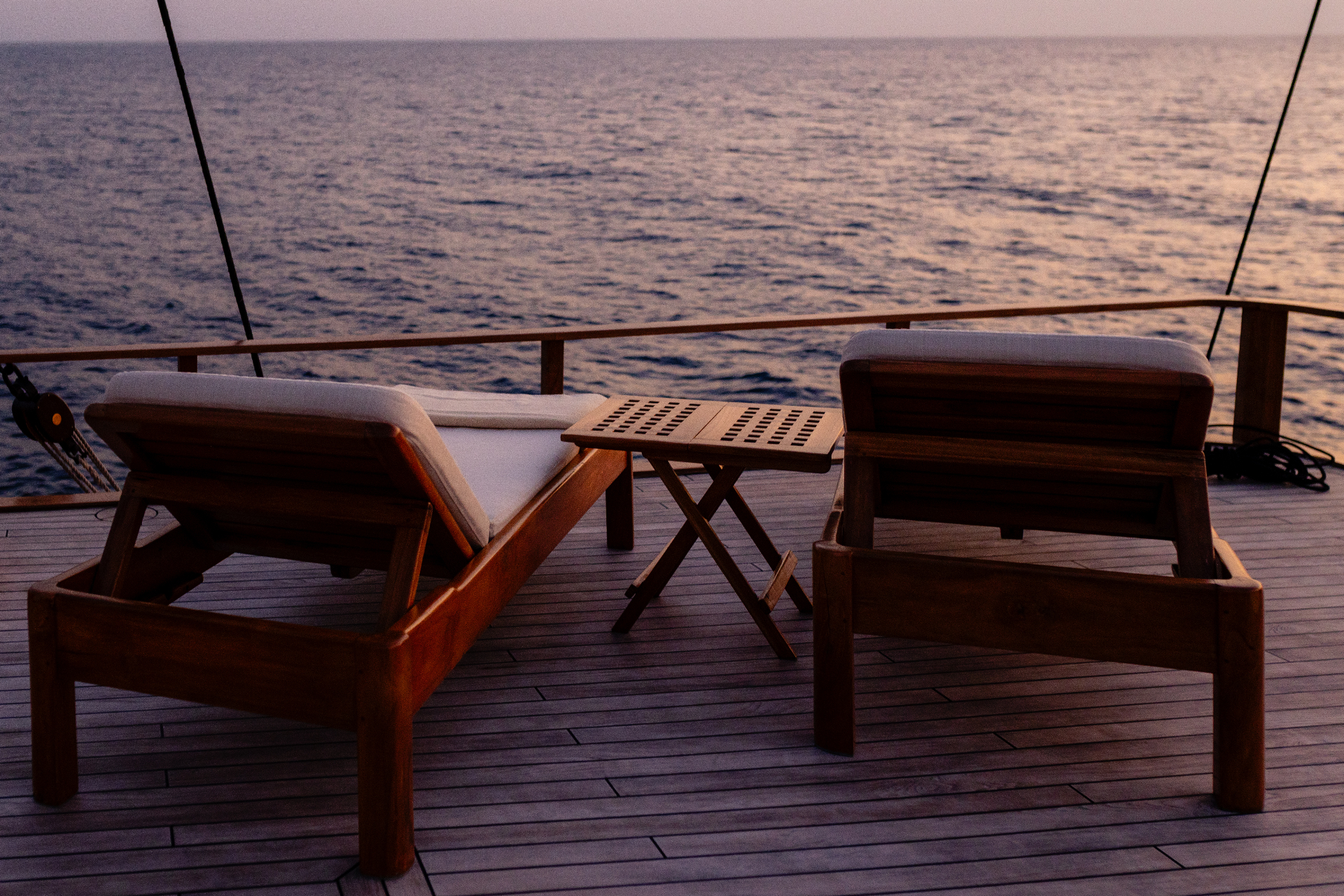 Two teak sun loungers on Silolona's deck at dusk over calm water