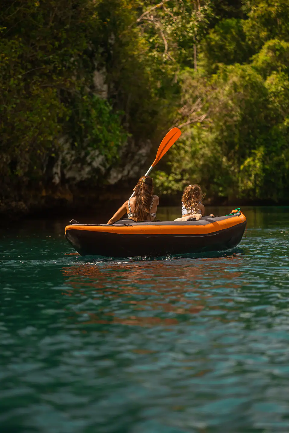 Mother and daughter kayaking along a jungle-lined shore during a Mutiara Laut charter