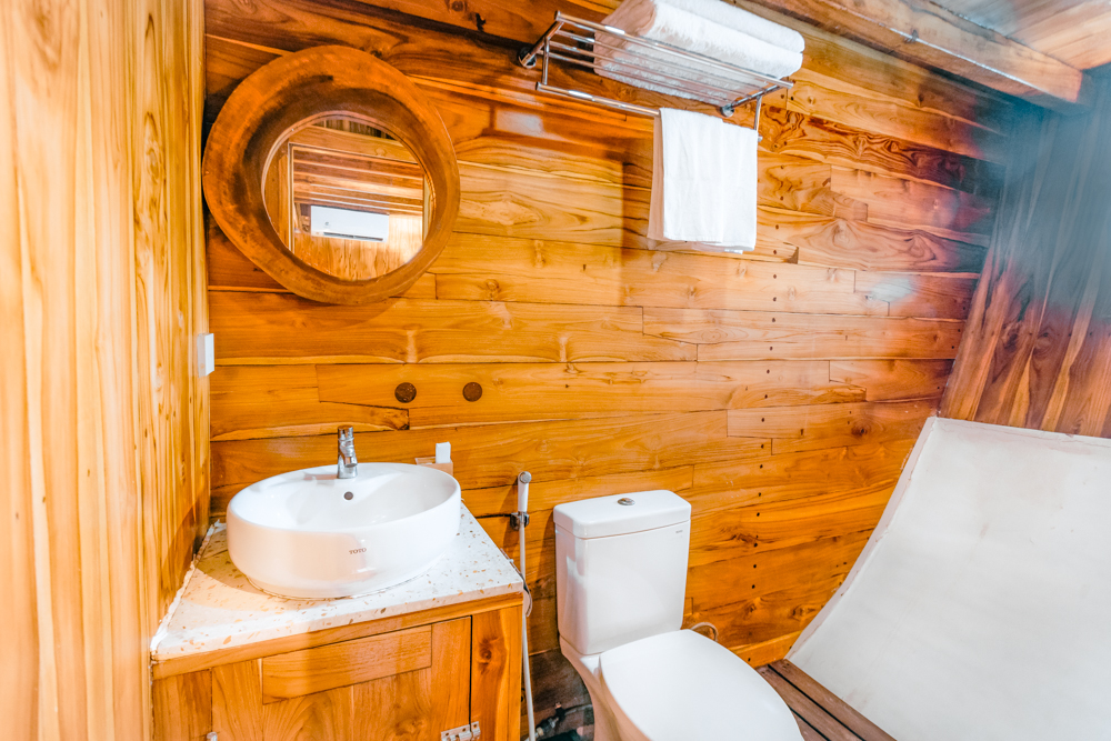 Andamari ensuite bathroom with round mirror, vessel sink, toilet and teak walls