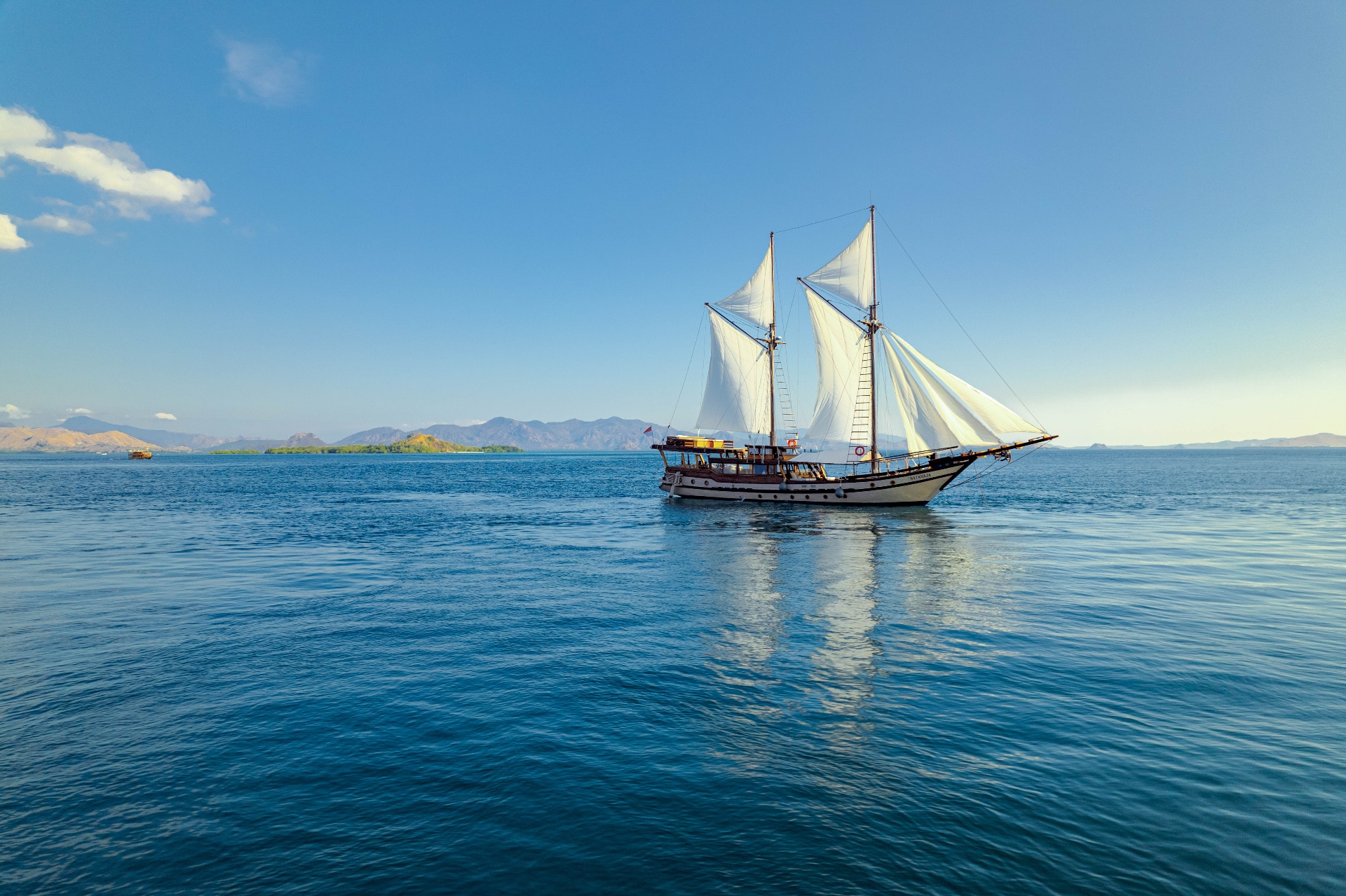 Nataraja sailing on glassy blue water with distant Komodo mountains behind