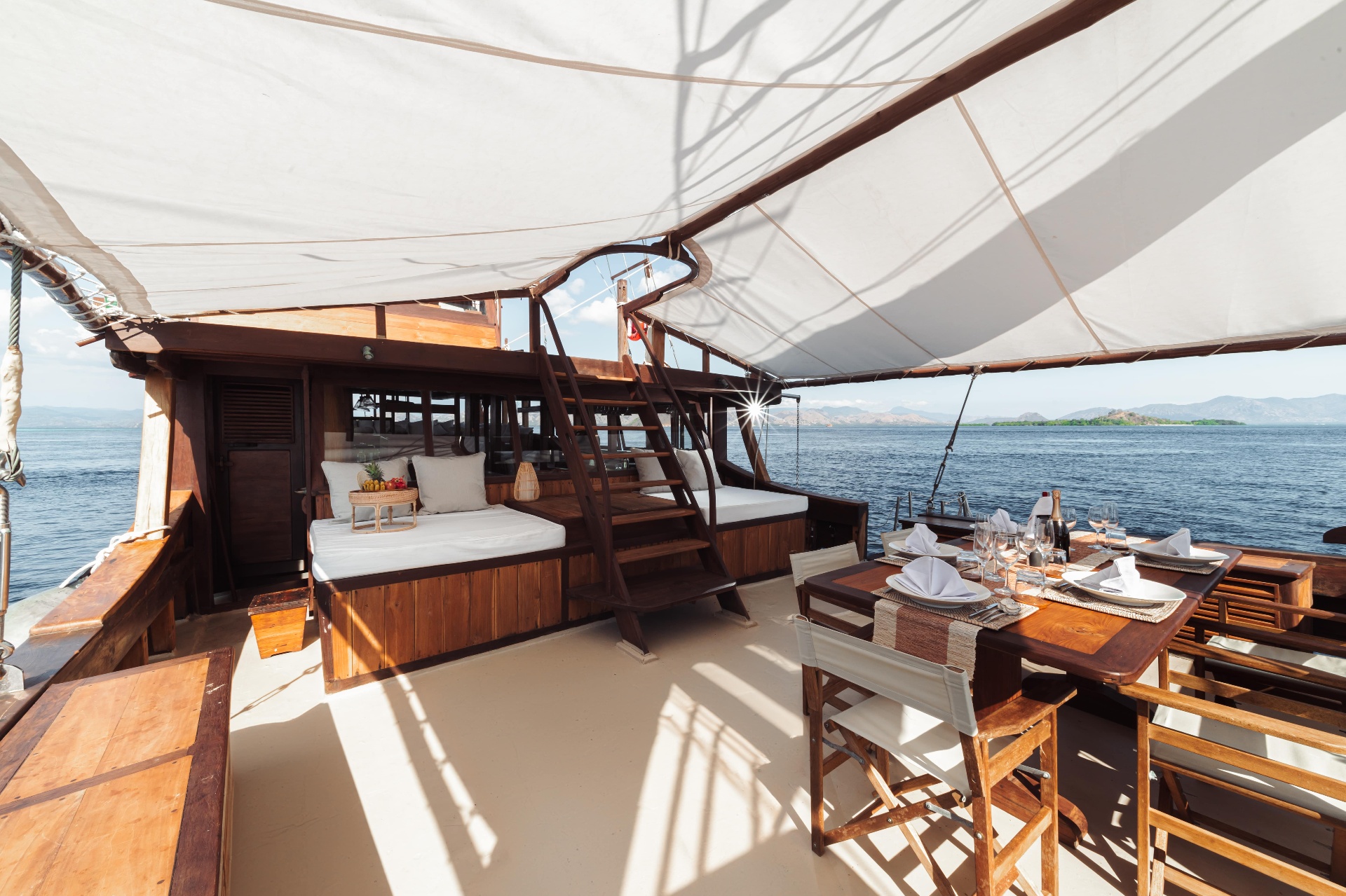 Foredeck on Nataraja with cushioned daybeds and a set dining table under a white sun sail