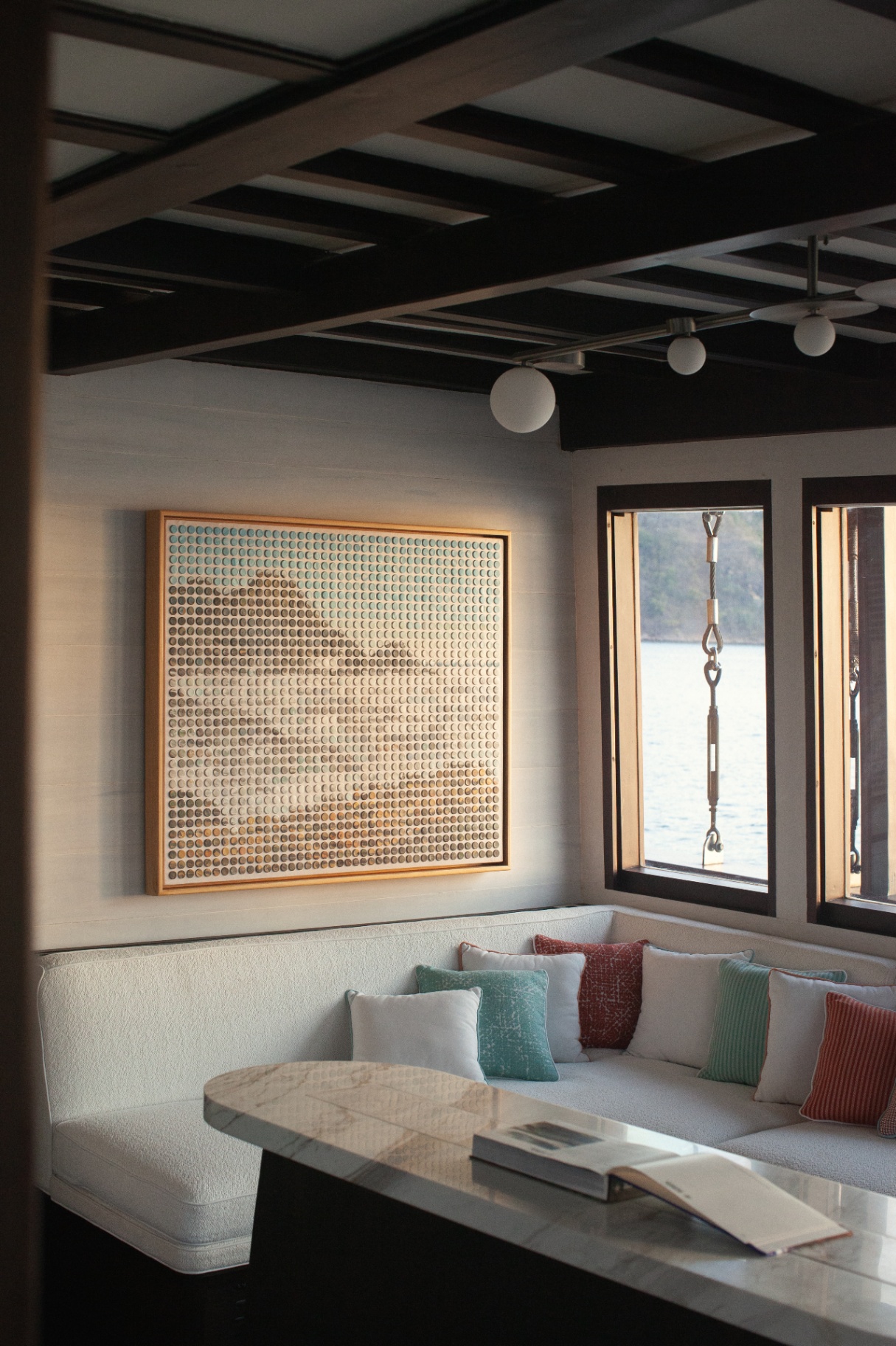 Saloon corner banquette on Vela with colorful cushions and a large framed dotted artwork on a linen wall
