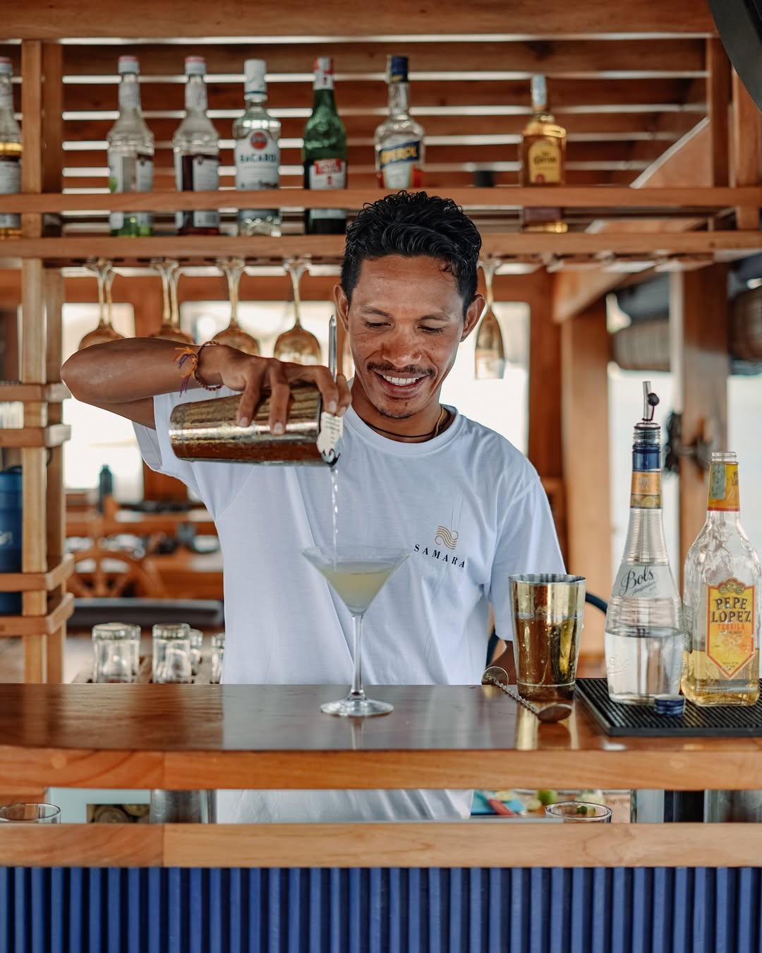 Samara II bartender in branded shirt pouring a cocktail into a martini glass at the onboard bar