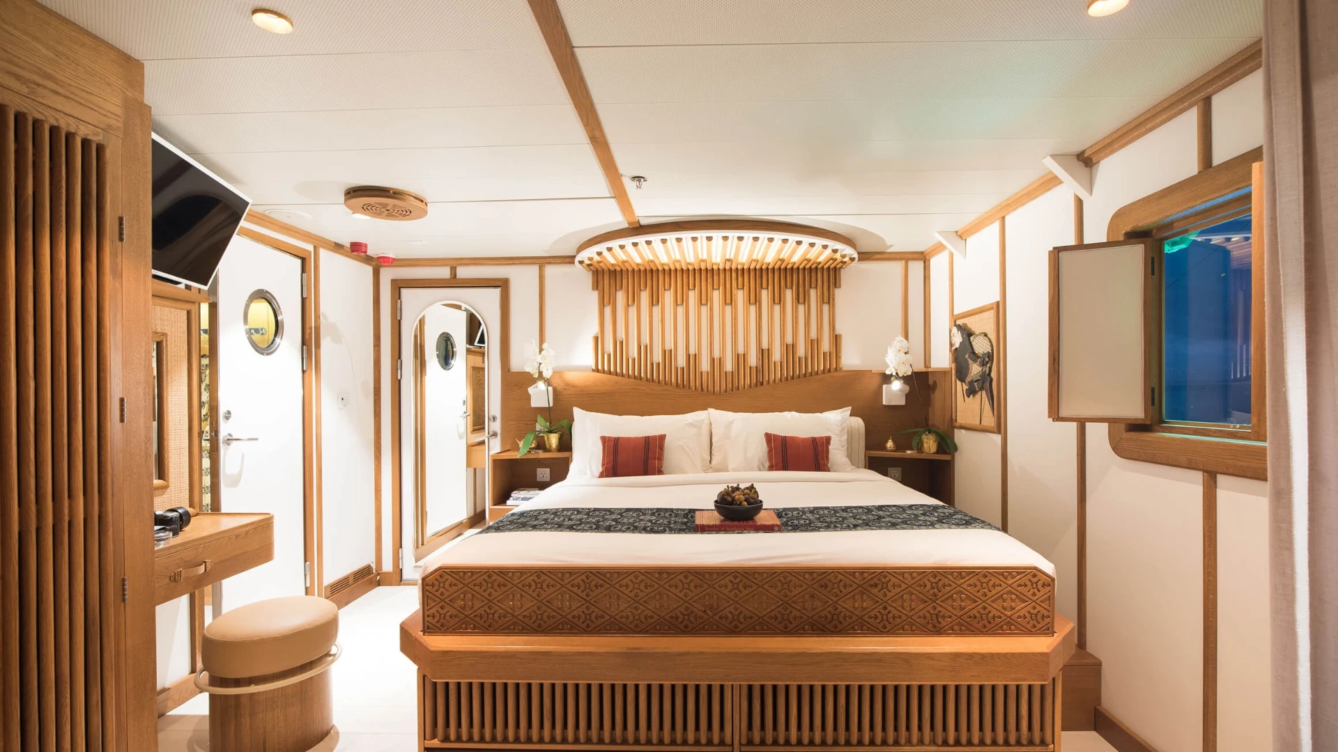 Above-deck cabin on Kudanil Explorer with king bed, carved timber headboard and porthole window