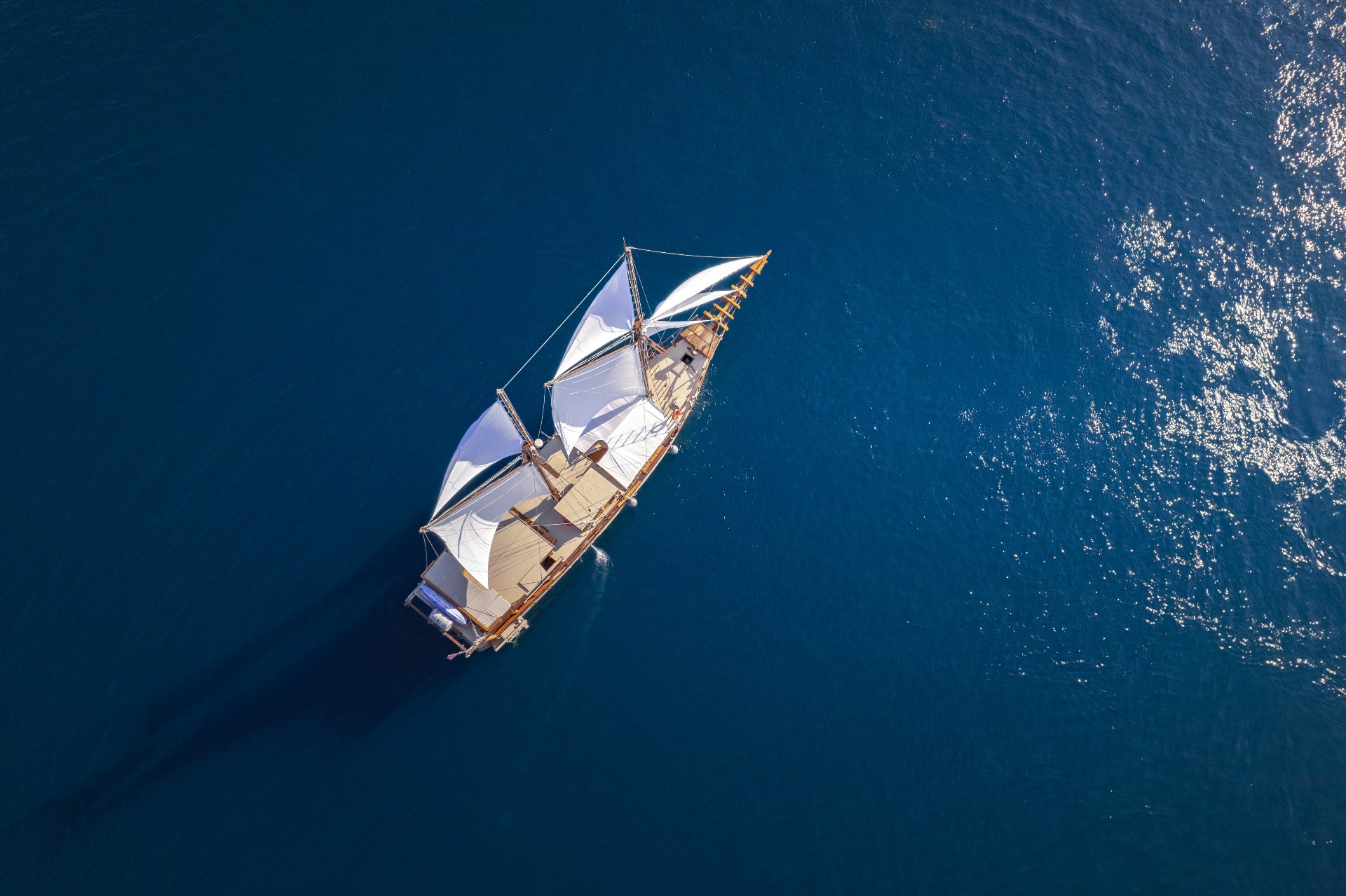 Top-down aerial of Nataraja under sail on deep blue water