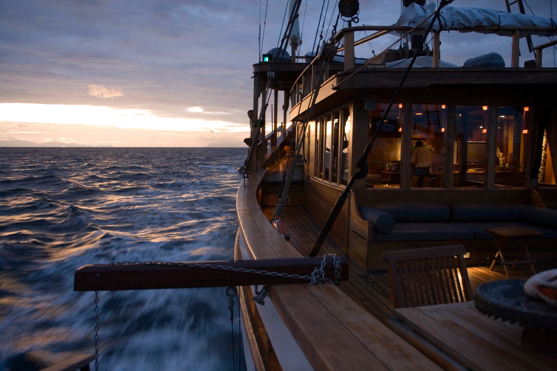 Silolona underway at dusk with saloon windows glowing warm over a rolling sea