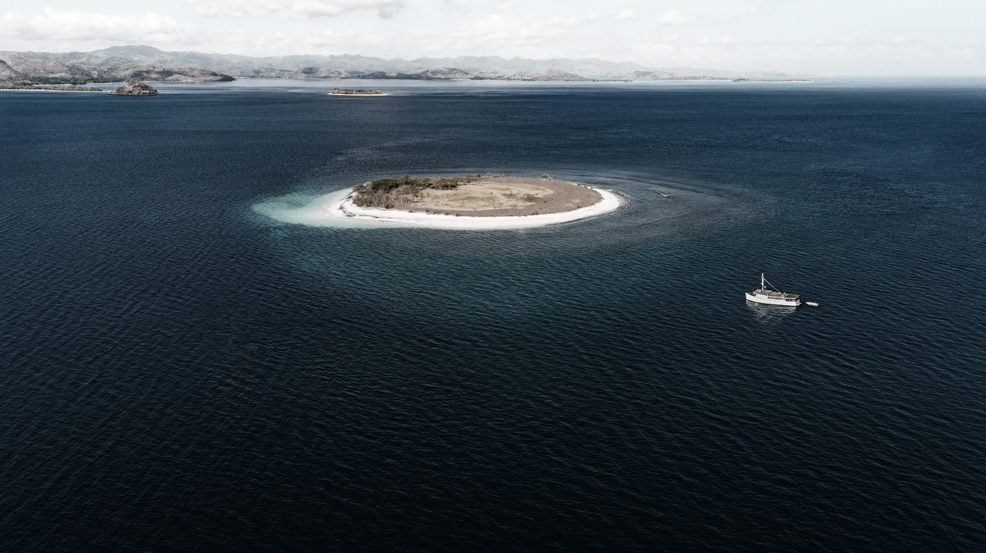 Splendour anchored beside a small sandy island ringed by turquoise shallows in the Komodo archipelago