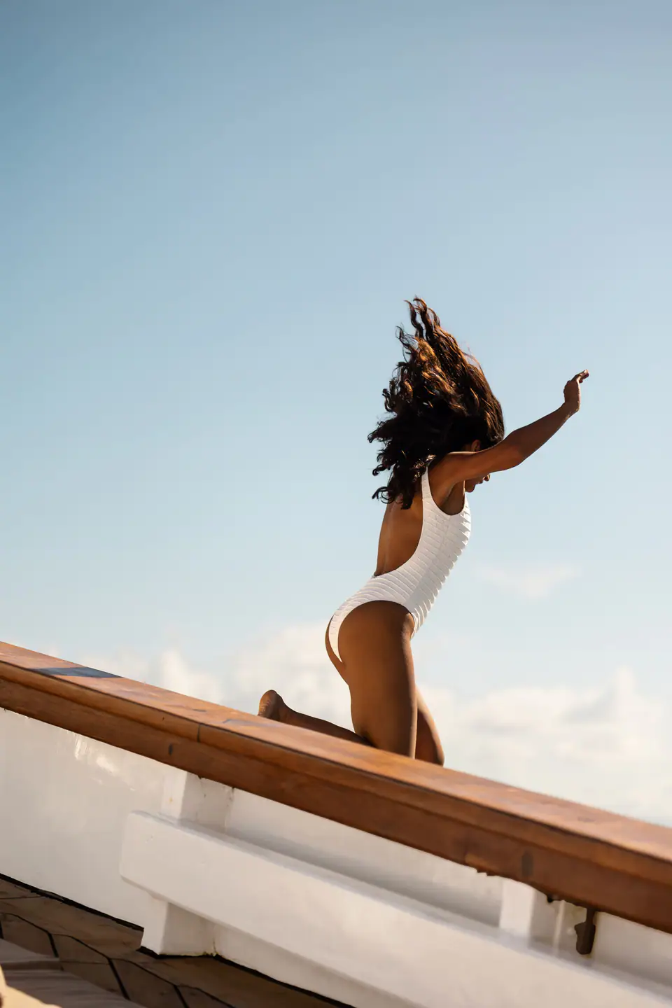Guest kneeling on Mutiara Laut's teak bulwark against bright blue sky