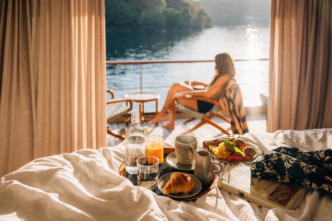 In-cabin breakfast tray with guest reading on the private balcony at sunrise