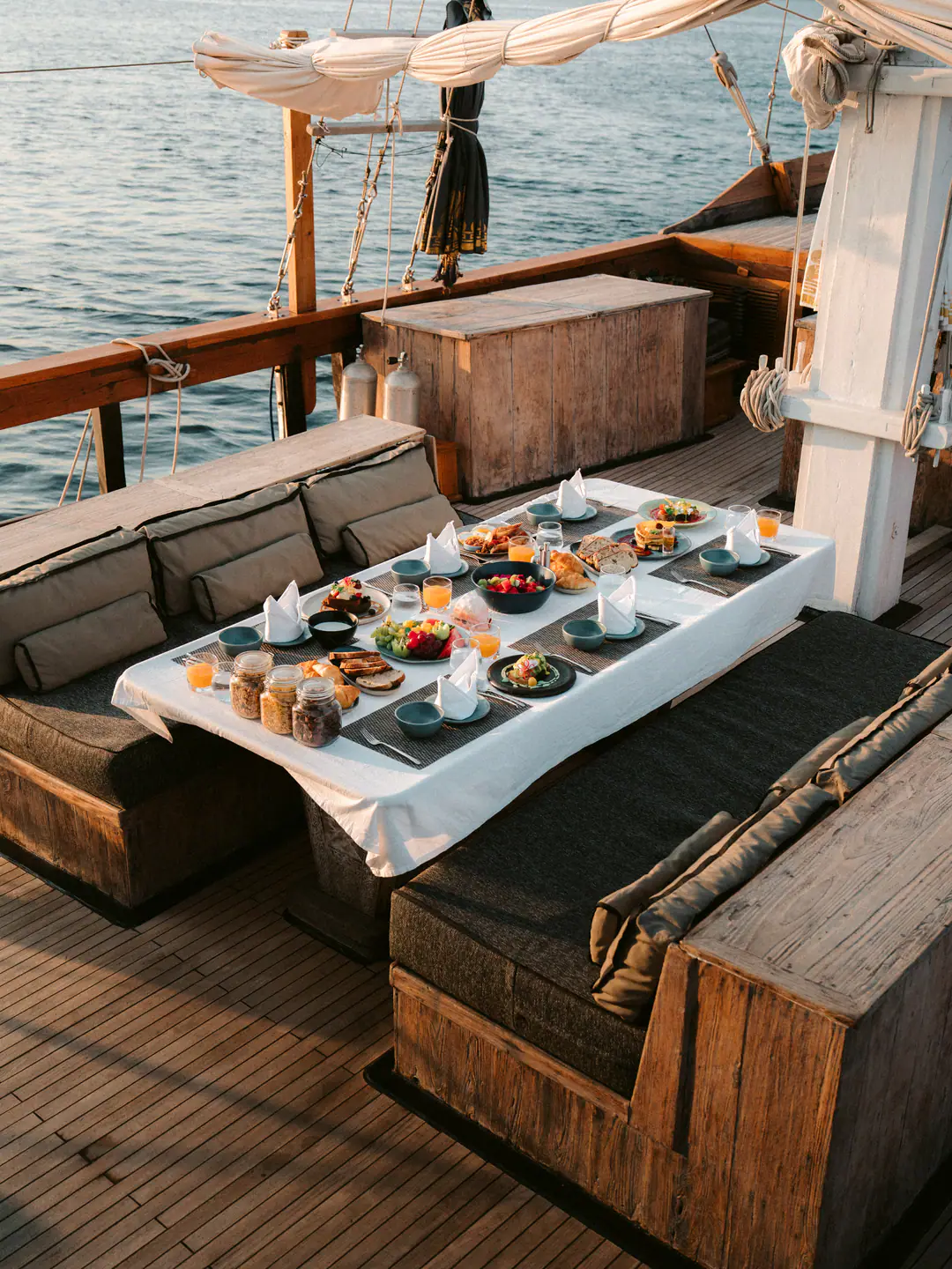 Long breakfast table laid out on The Oracle's shaded deck with sea alongside