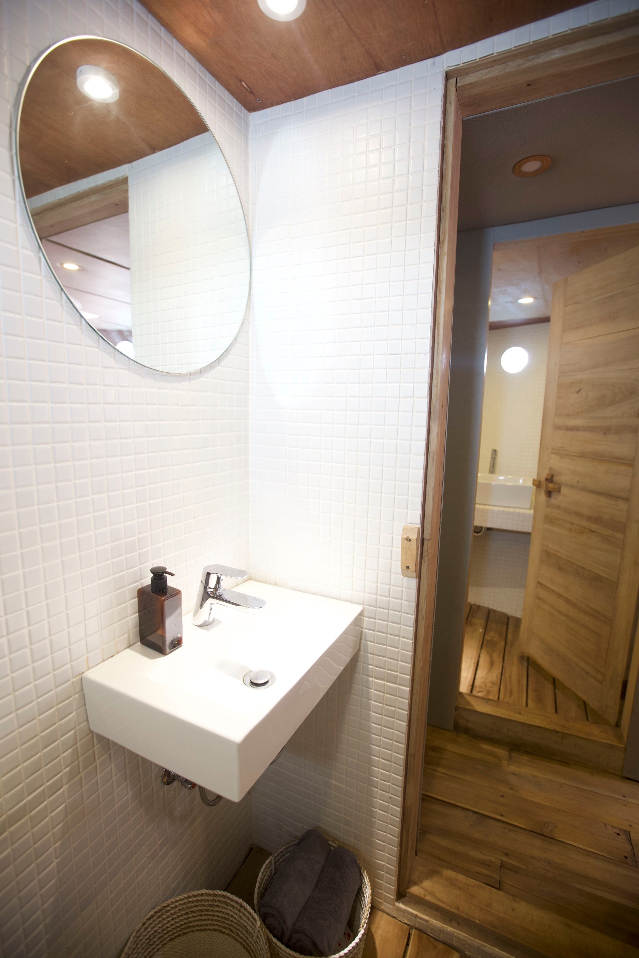 Splendour ensuite bathroom with white mosaic tiles, round mirror, wall-mounted basin and timber door