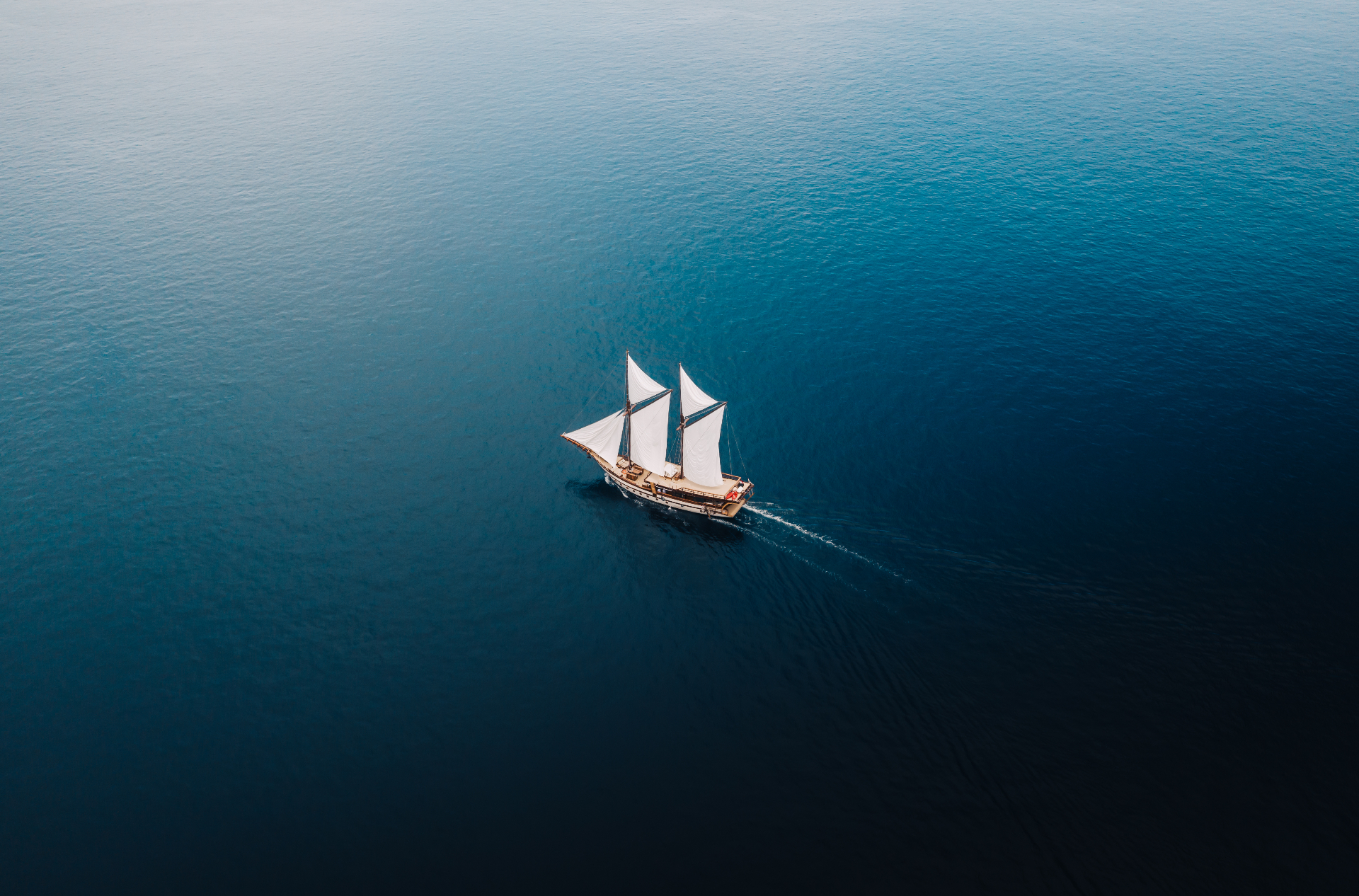 High aerial of Senja as a small silhouette under sail on endless deep blue sea
