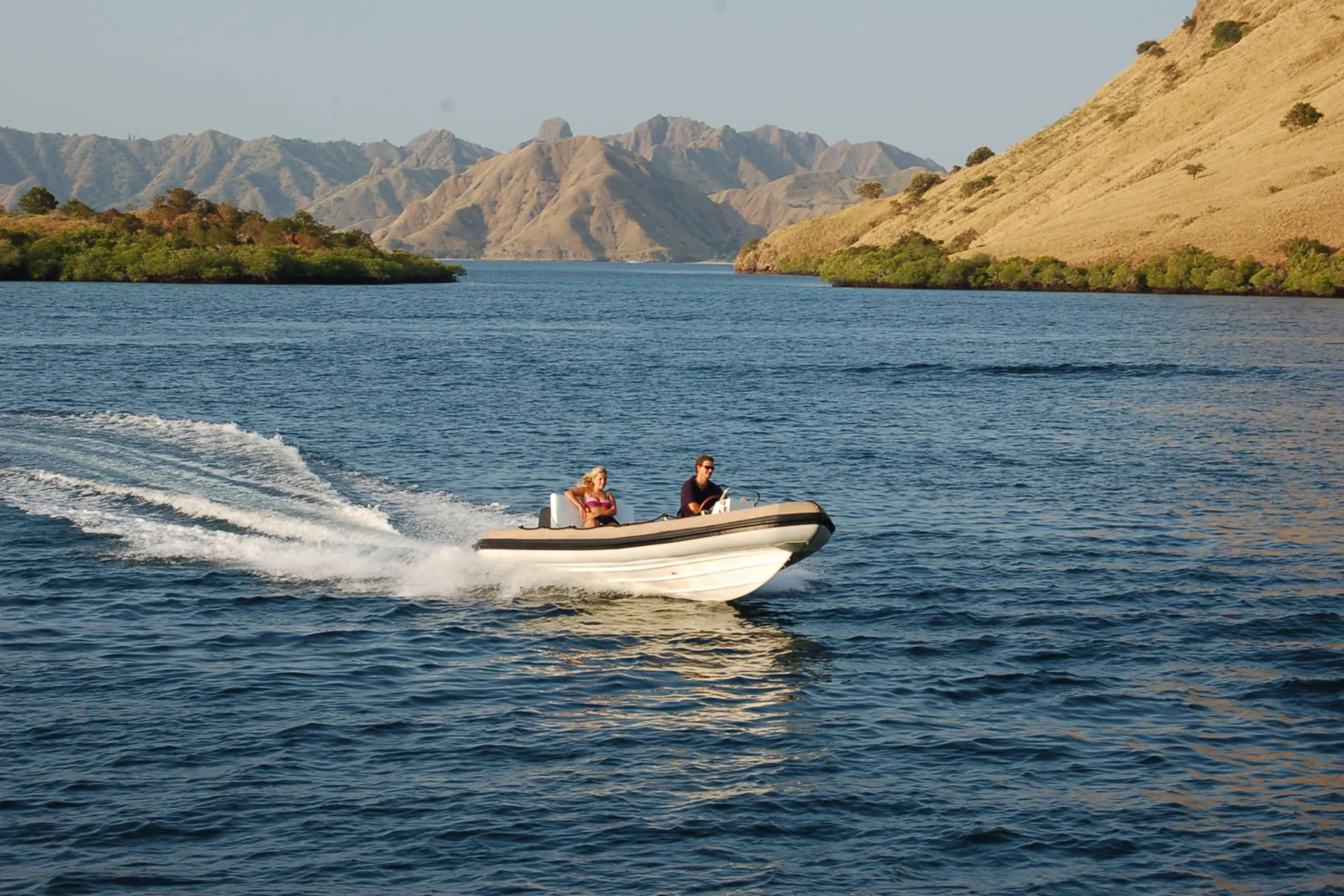 Guests cruising in Si Datu Bua's tender through Komodo channels with dry hills in the background