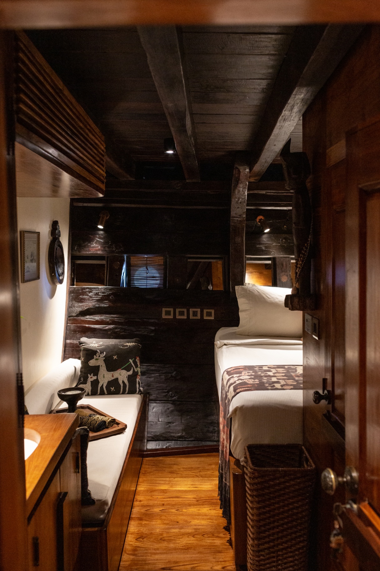 Twin cabin on Silolona with dark ironwood beams, ikat throws and a porthole
