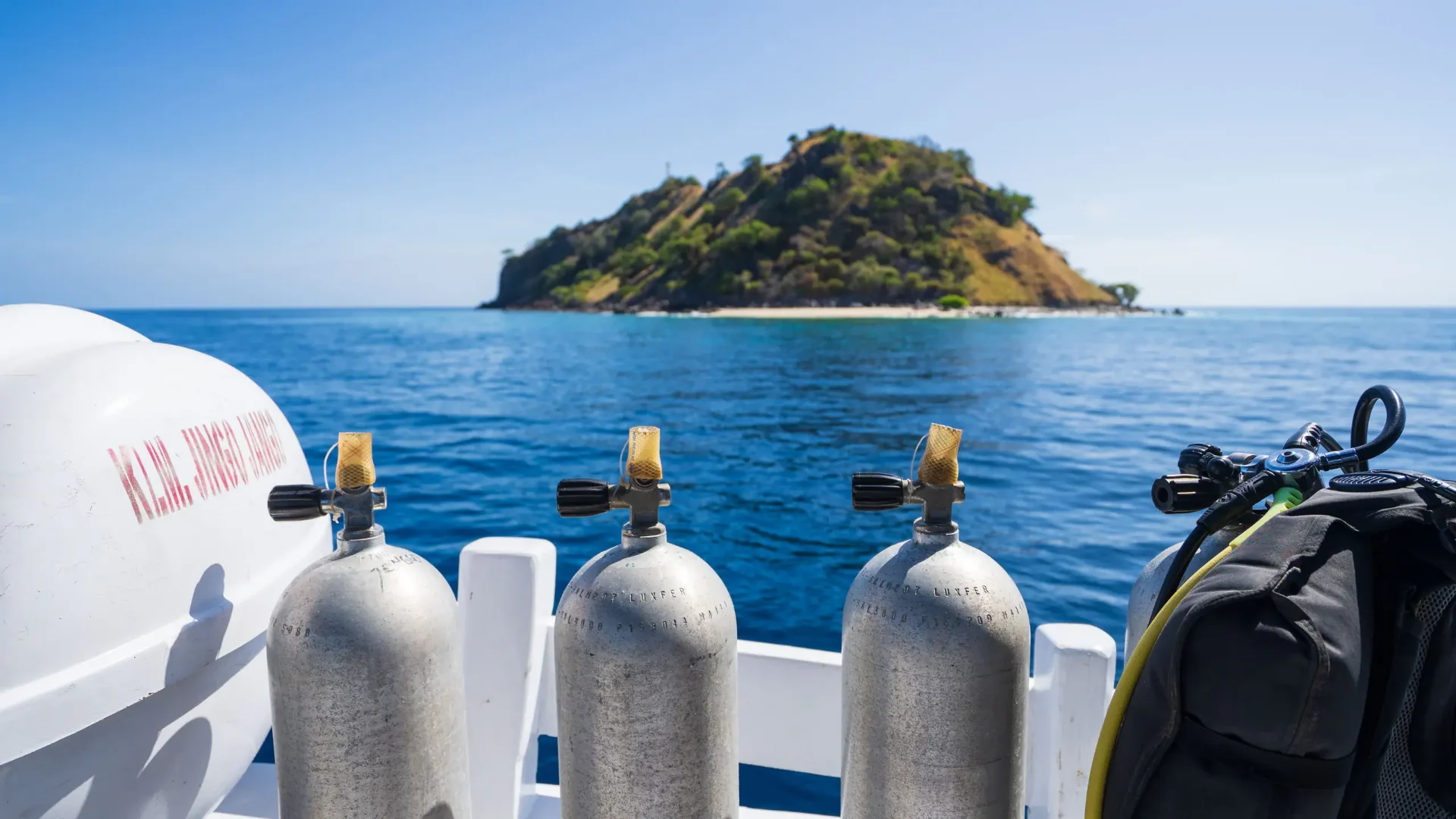 Row of dive tanks lined up on Jinggo Janggo's stern with a Komodo island beyond