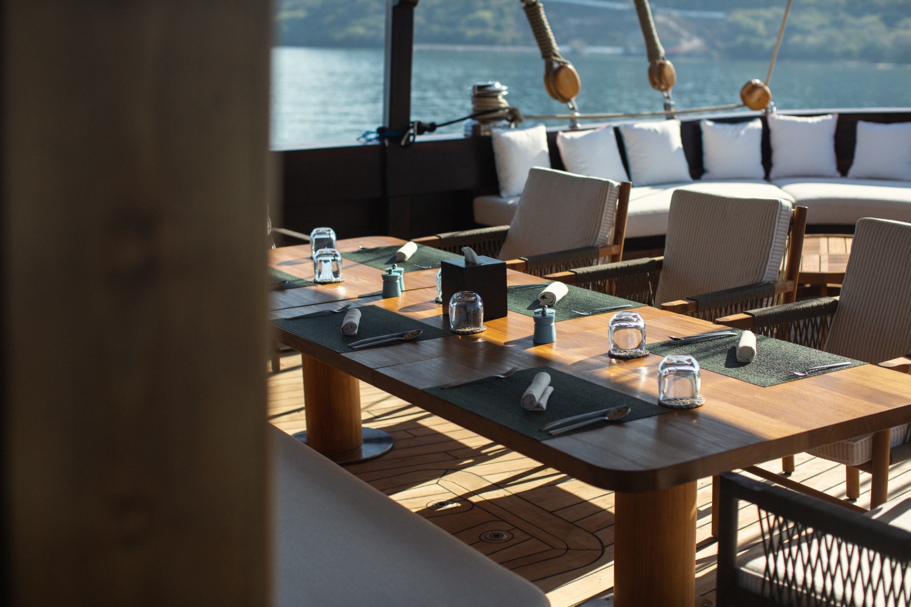 Vela's alfresco dining table set with placemats, glassware and rolled napkins on teak deck overlooking the sea