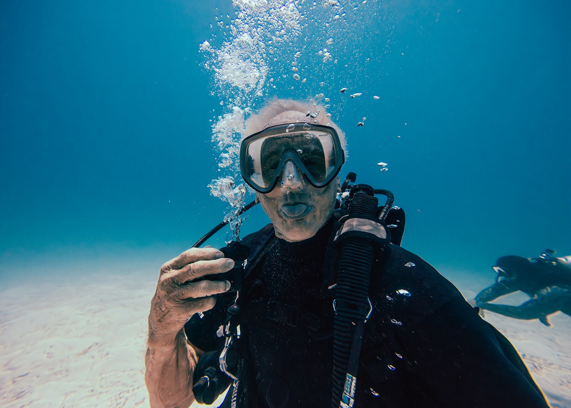 Scuba diver on a sandy bottom with a second diver in the distance