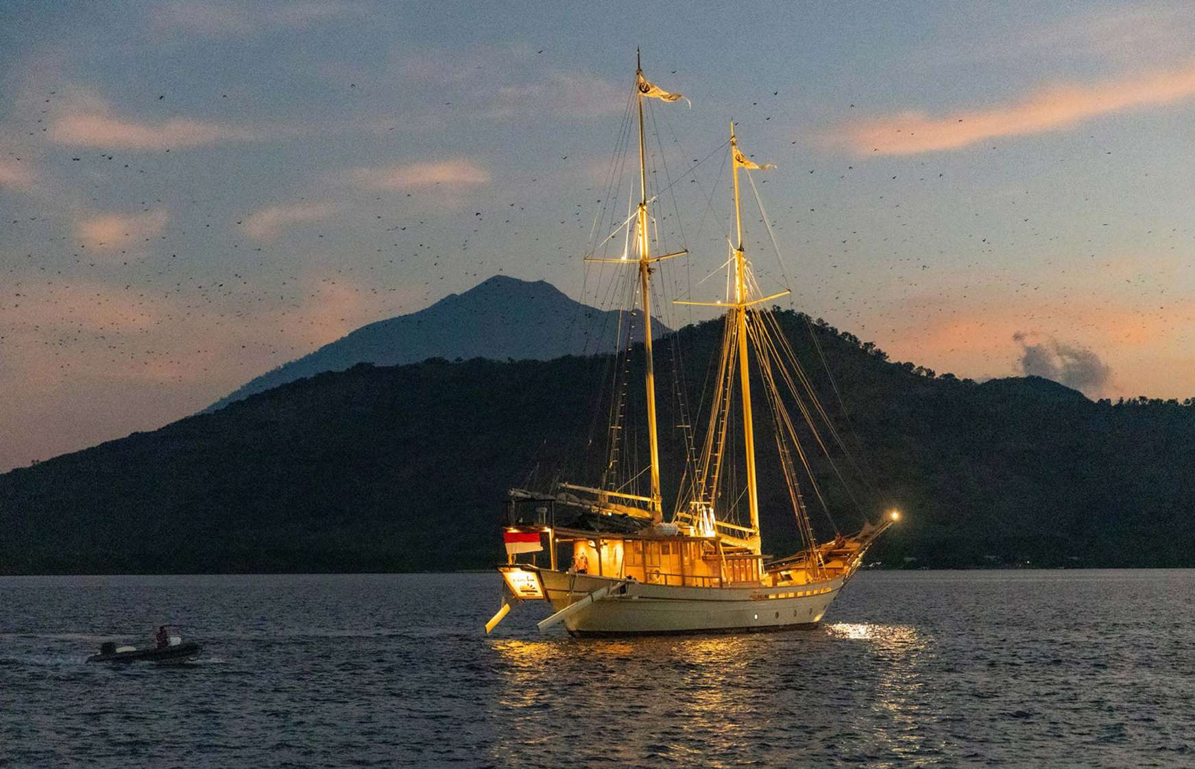 Si Datu Bua anchored at dusk in a calm bay with a large mountain behind