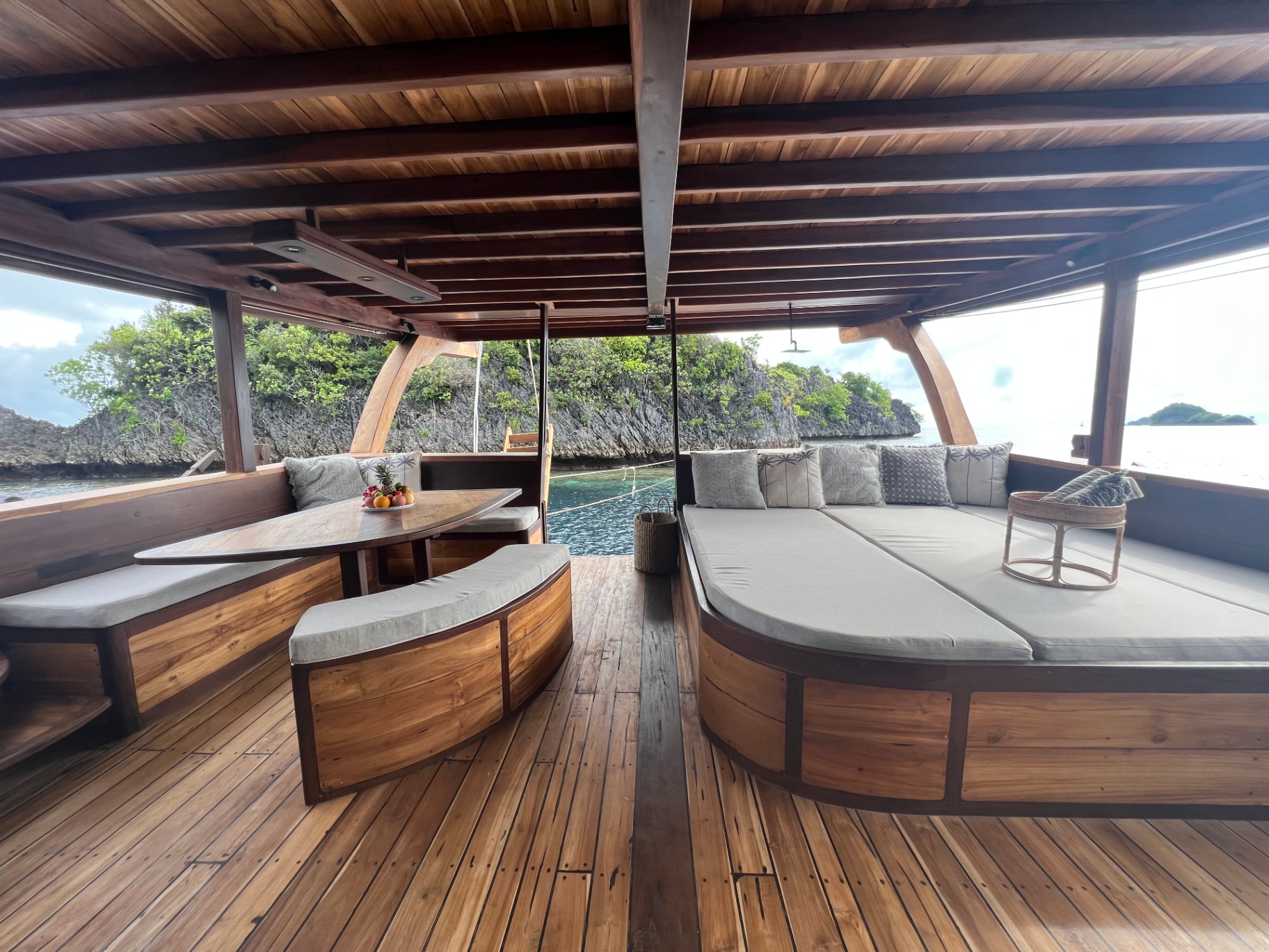 Dewata chill deck with dining table and large daybed inside a karst-lined bay