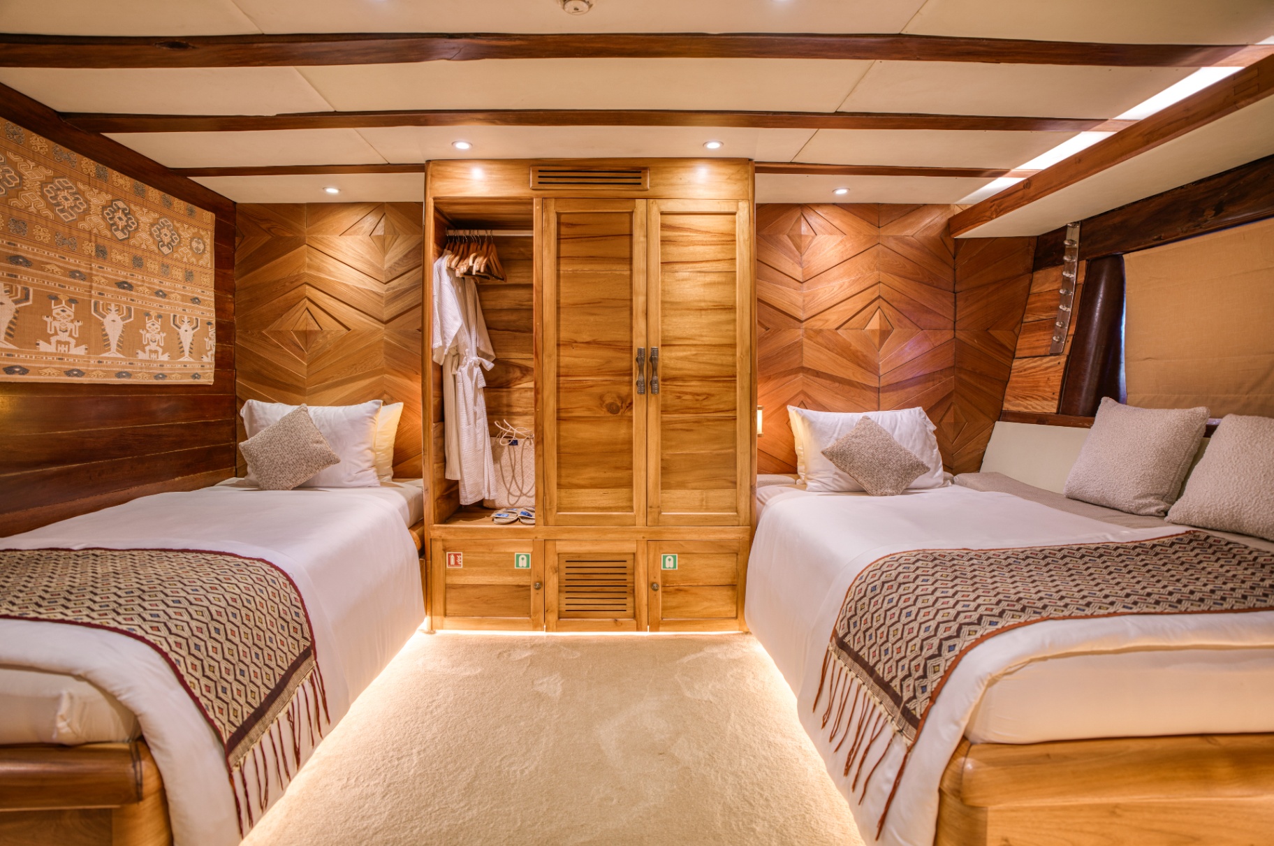 Lamima twin cabin with two single beds flanking a central teak wardrobe and woven textile art