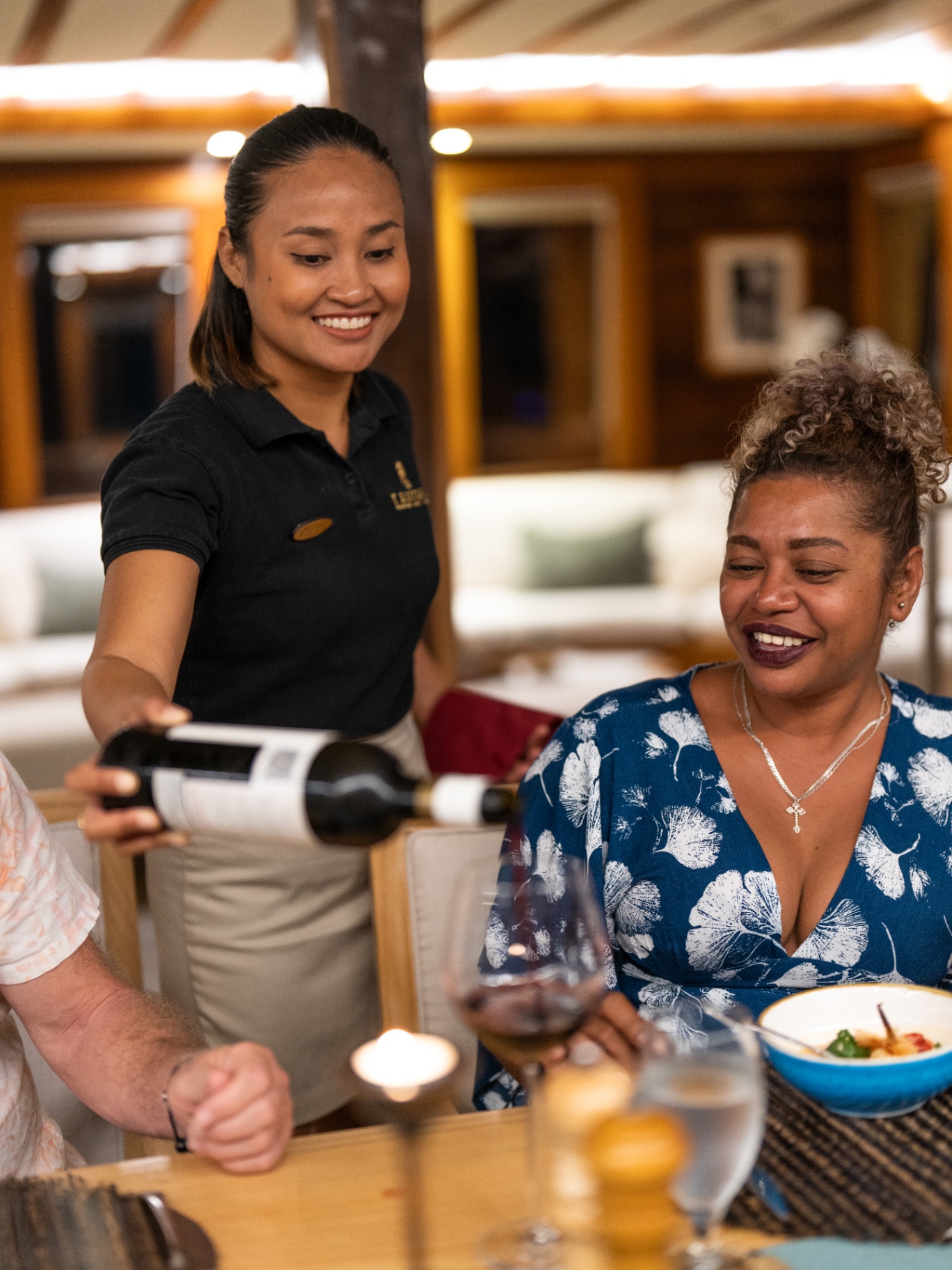 Lamima crew member pouring wine for smiling guest during dinner service in the saloon