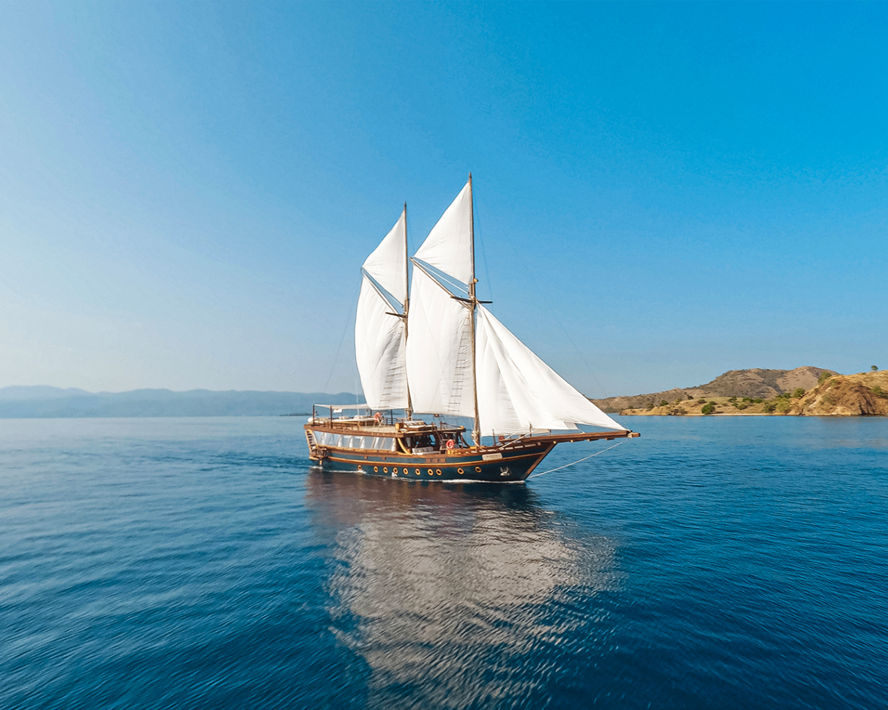 Sanya phinisi sailing under full white sails on bright blue water
