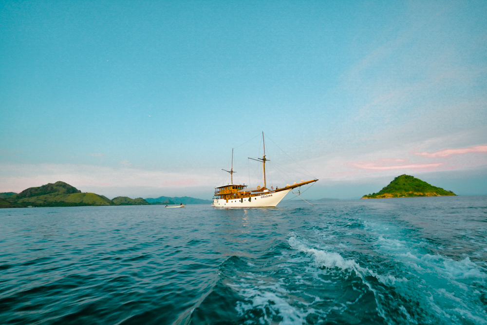 Adishree seen from a tender at sunset with two masts silhouetted against pastel sky