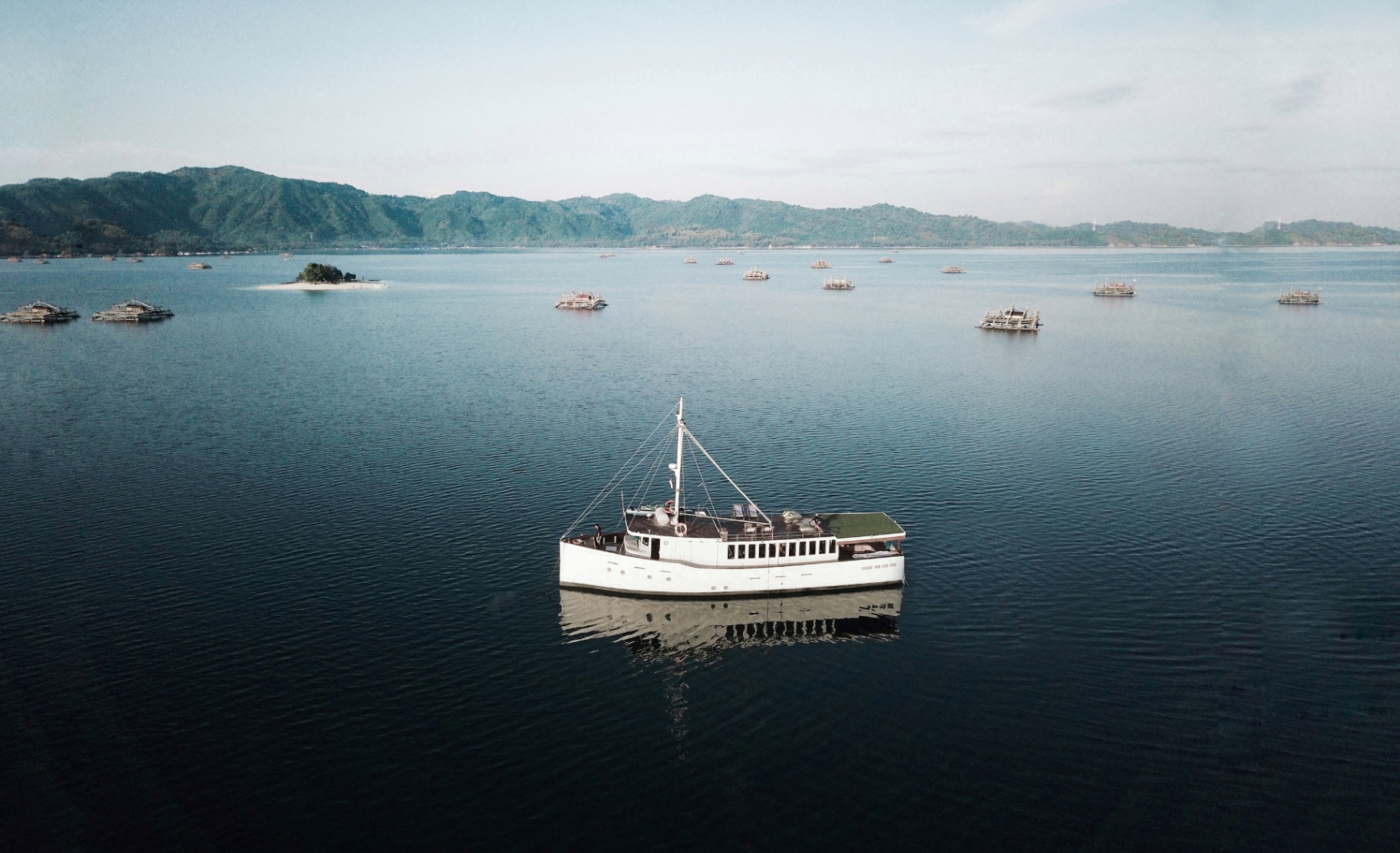 Splendour anchored on glassy water at dawn beside a small island with fishing platforms in the distance