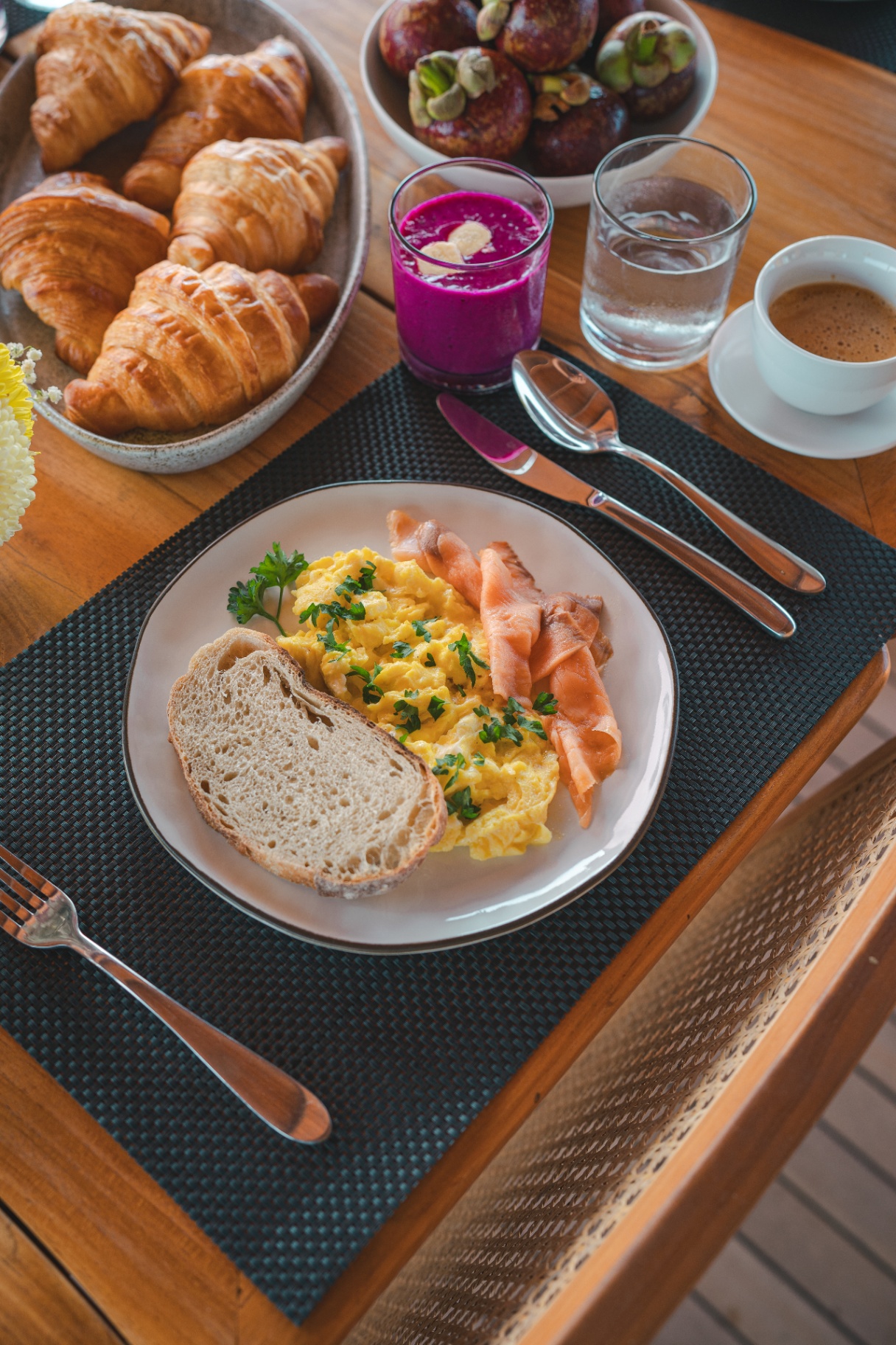 Full breakfast setting on Mischief with eggs, salmon, croissants, dragon fruit smoothie, coffee and mangosteen