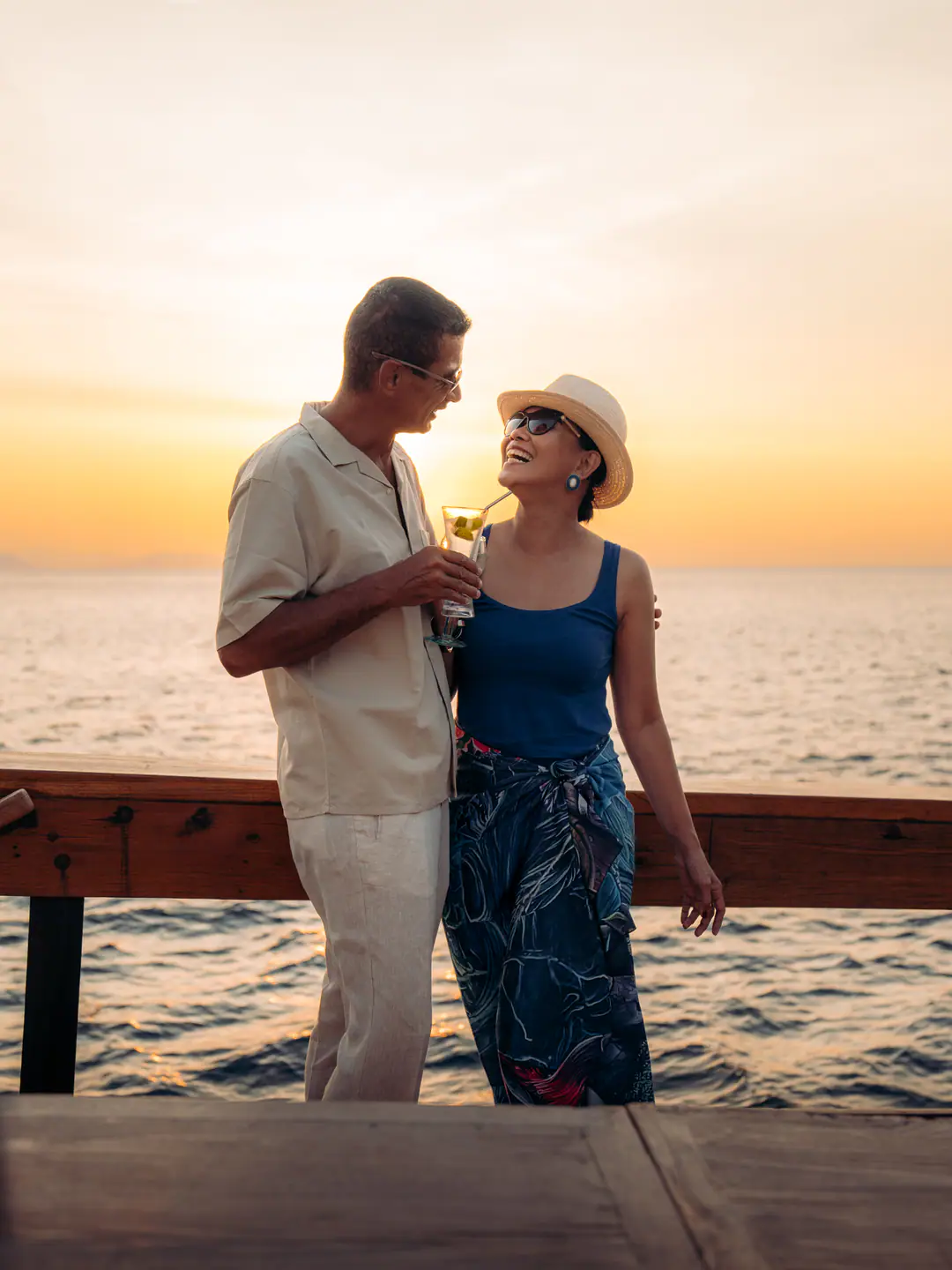 Couple sharing a cocktail at sunset on The Oracle's deck over calm sea