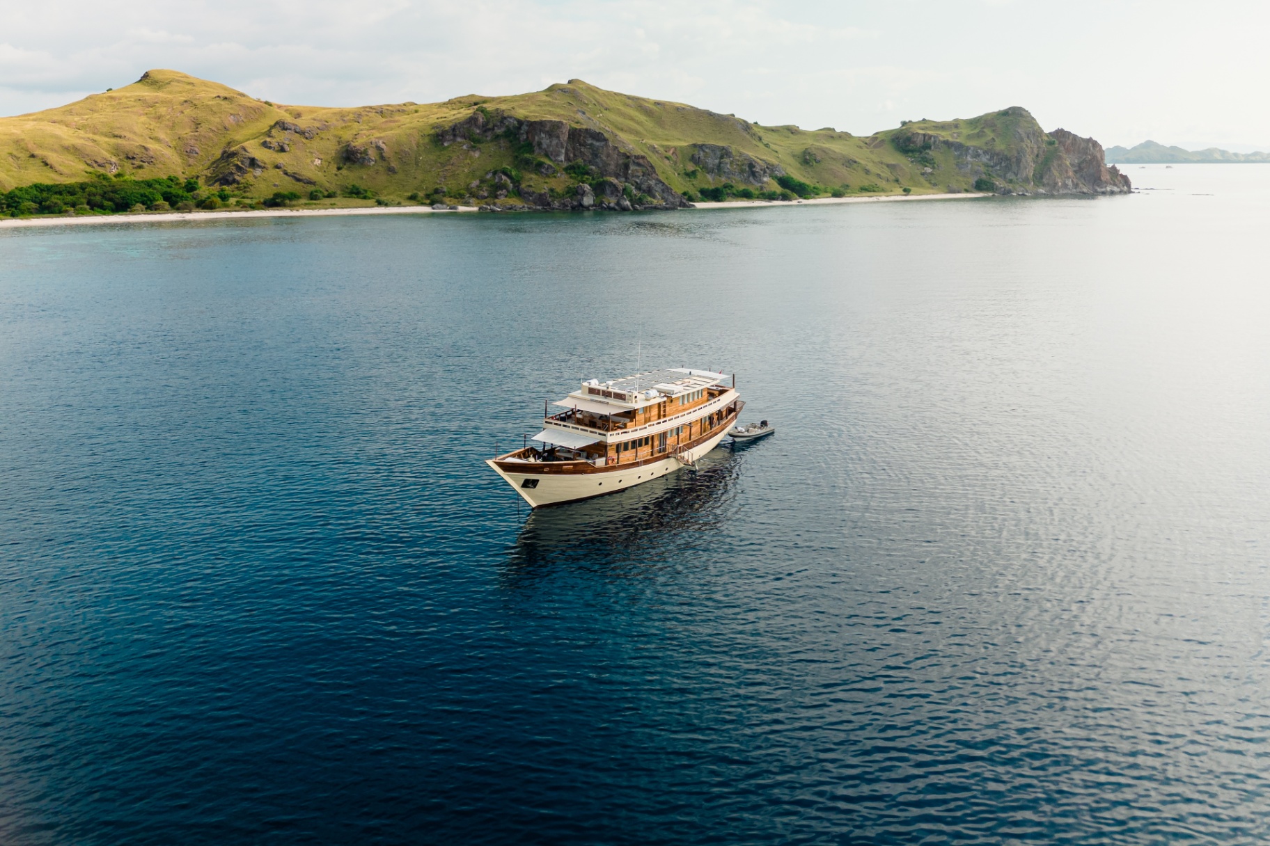 Mischief cruising past a golden Komodo island with tender in tow