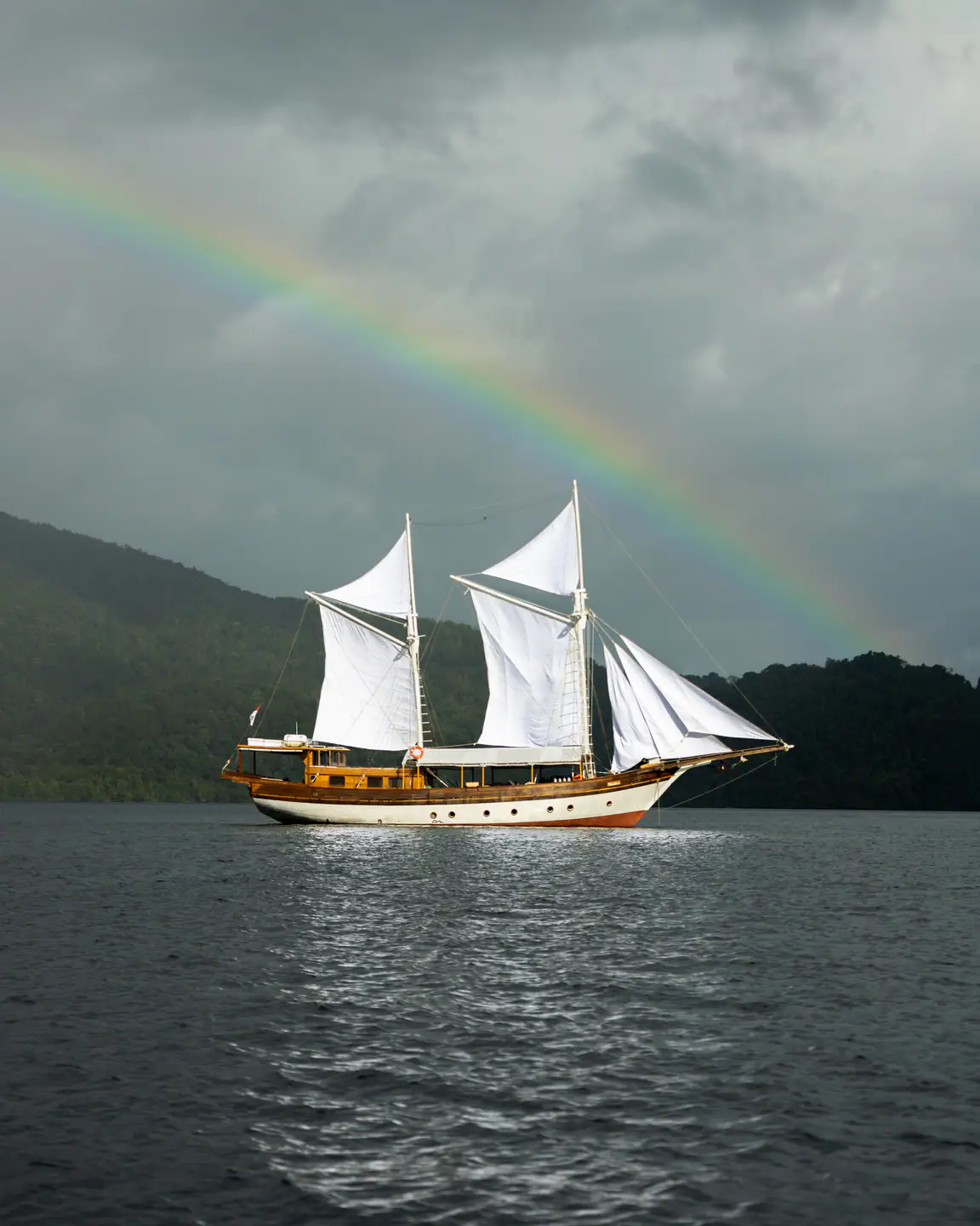 Anne Bonny phinisi sailing under a rainbow in Raja Ampat