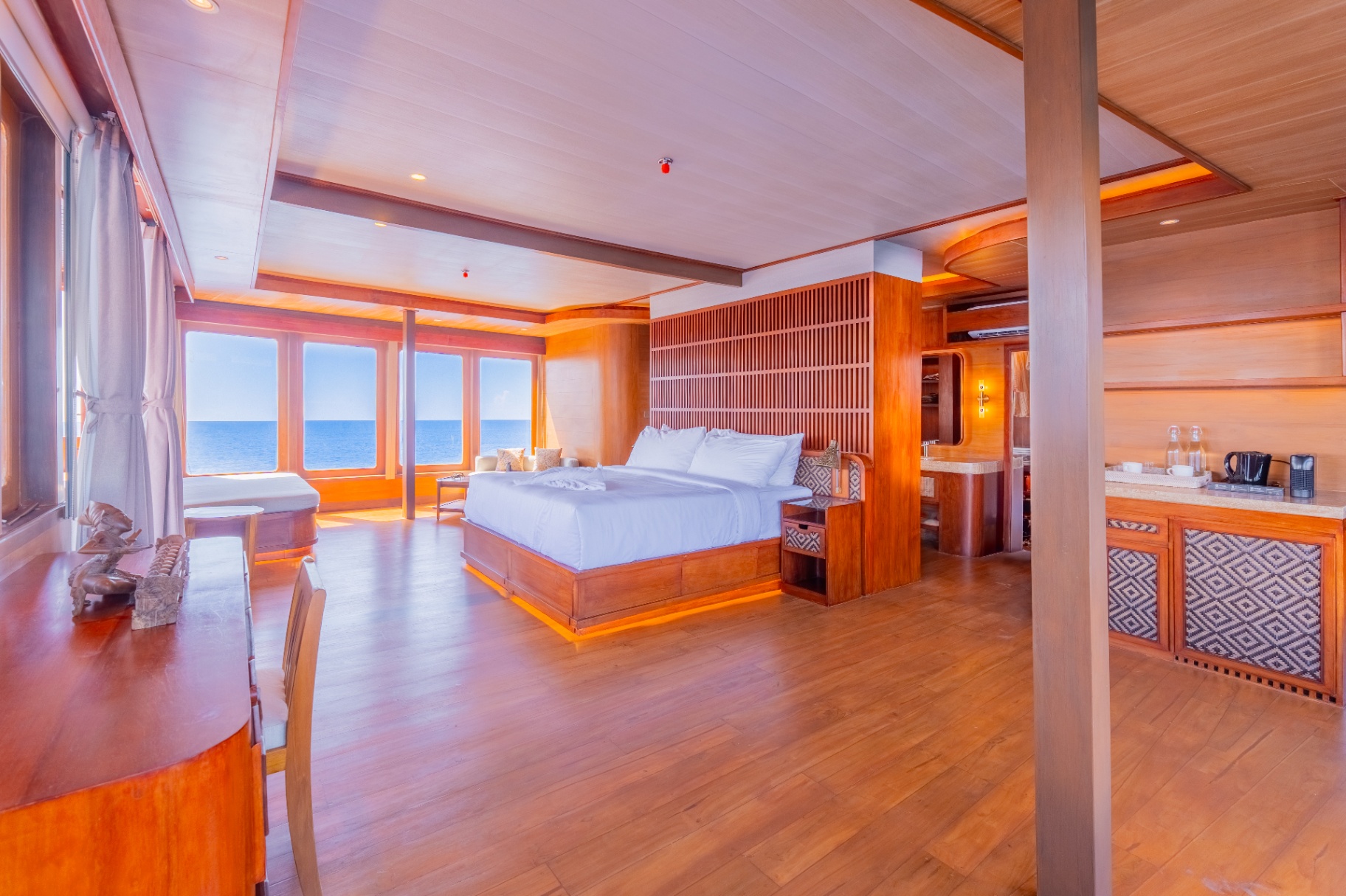 Wide view of Sanctuary's master suite with king bed, lounge area and Nespresso bar under a slatted teak headboard wall