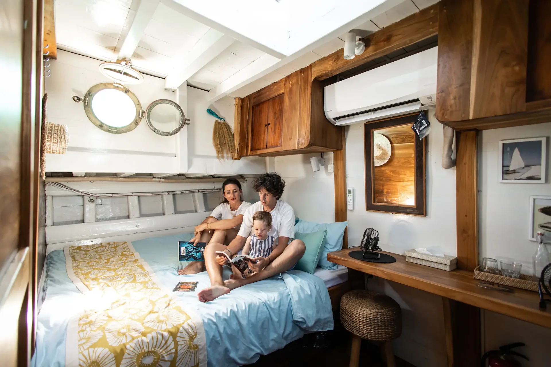 Family relaxing in a Jinggo Janggo cabin with porthole windows and teak trim