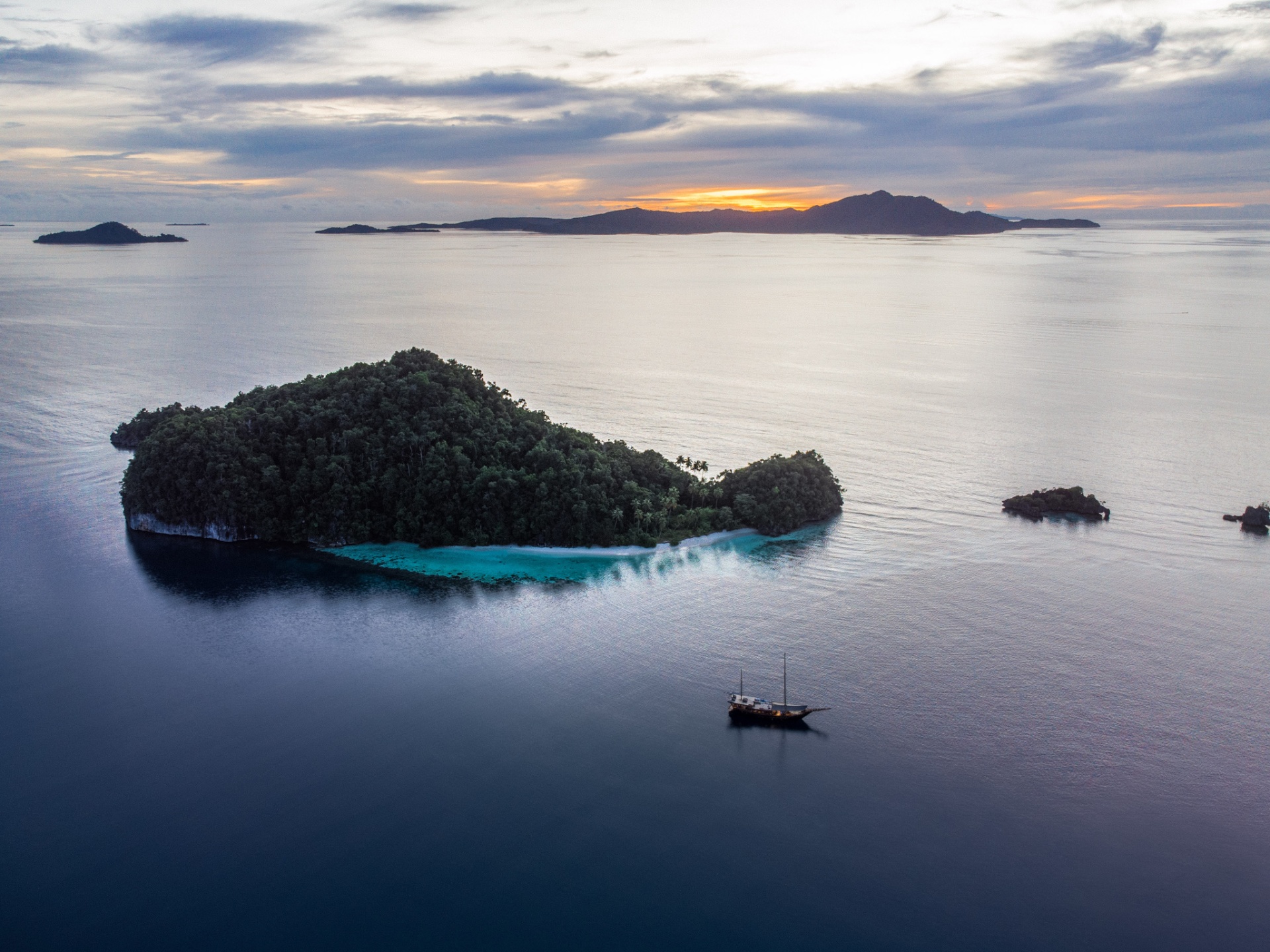 Senja phinisi anchored beside a jungle-clad island at sunset in Raja Ampat