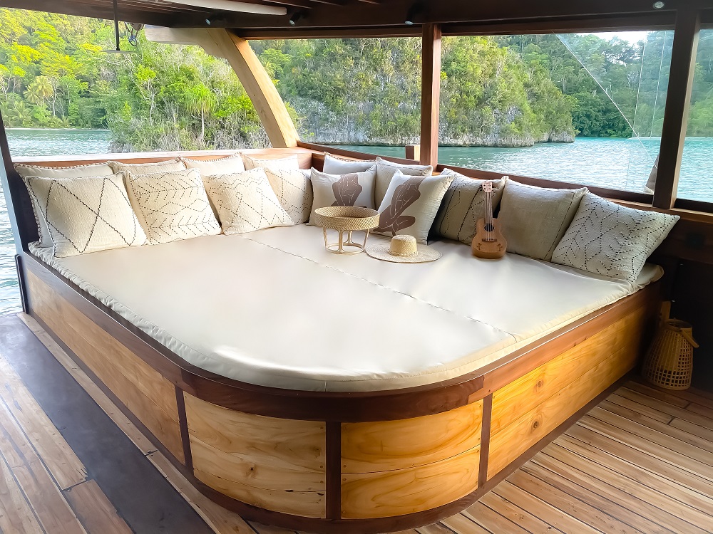 Large outdoor daybed on Senja piled with cushions, opening to a Raja Ampat lagoon
