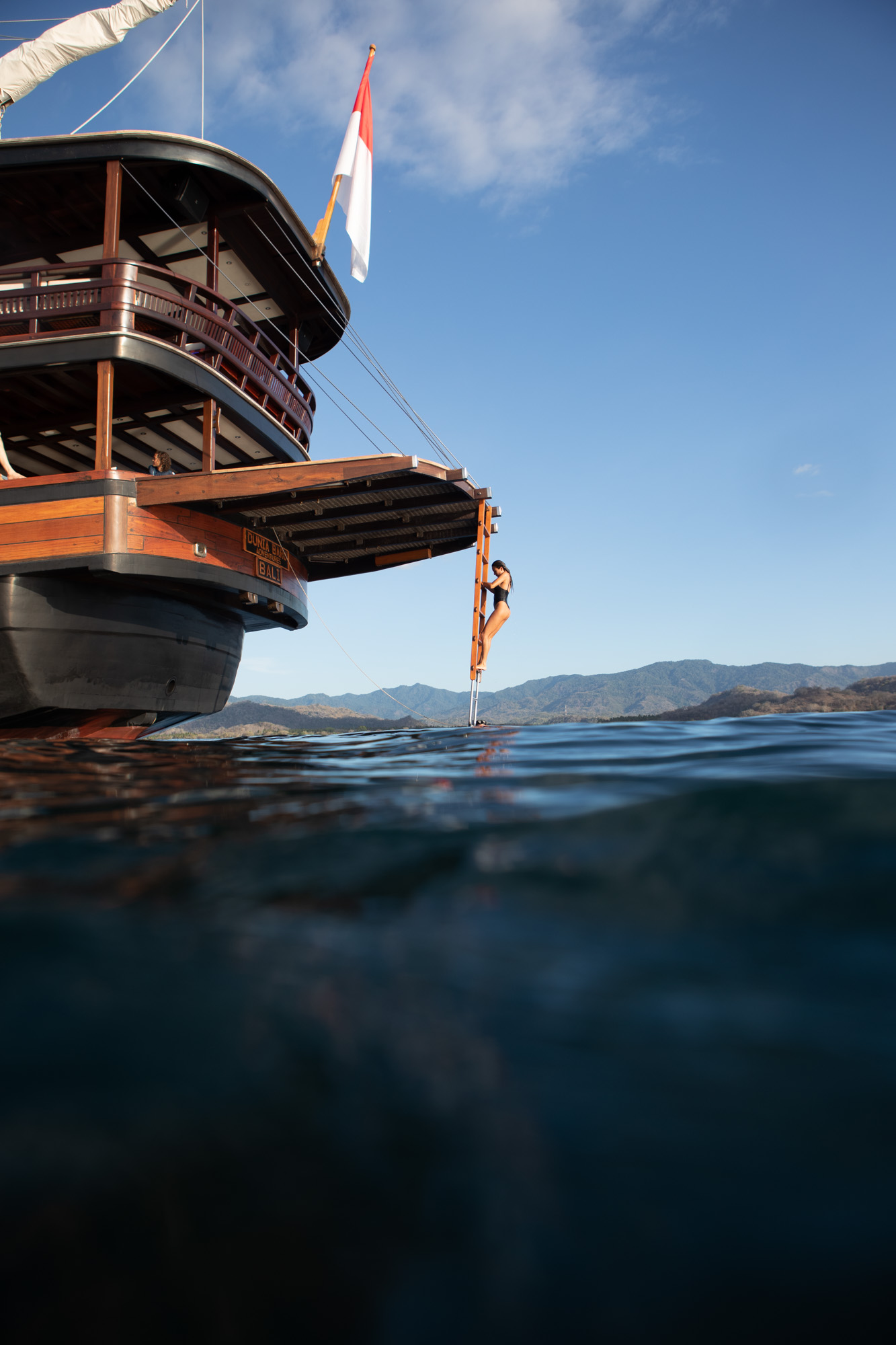 Guest climbing the aft swim ladder of Dunia Baru with Indonesian flag flying