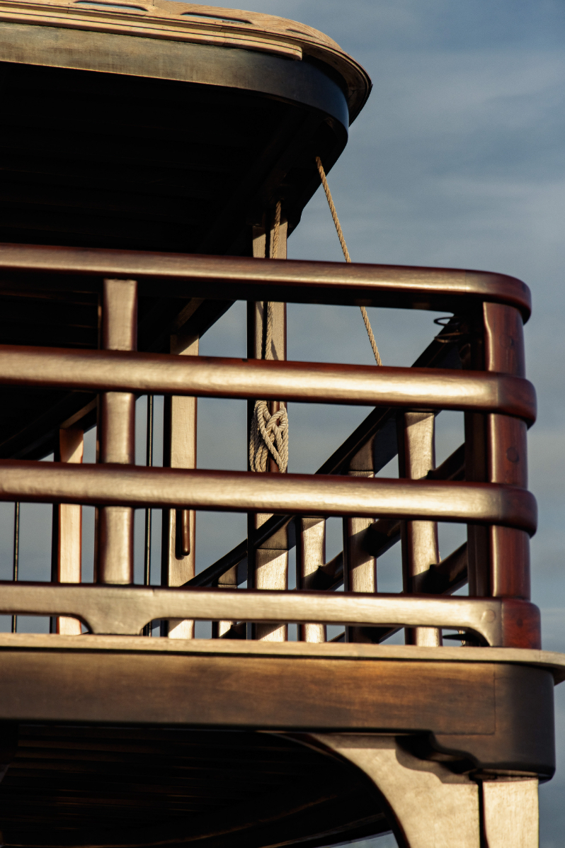 Close-up of curved teak railings and hand-tied rope at sunset
