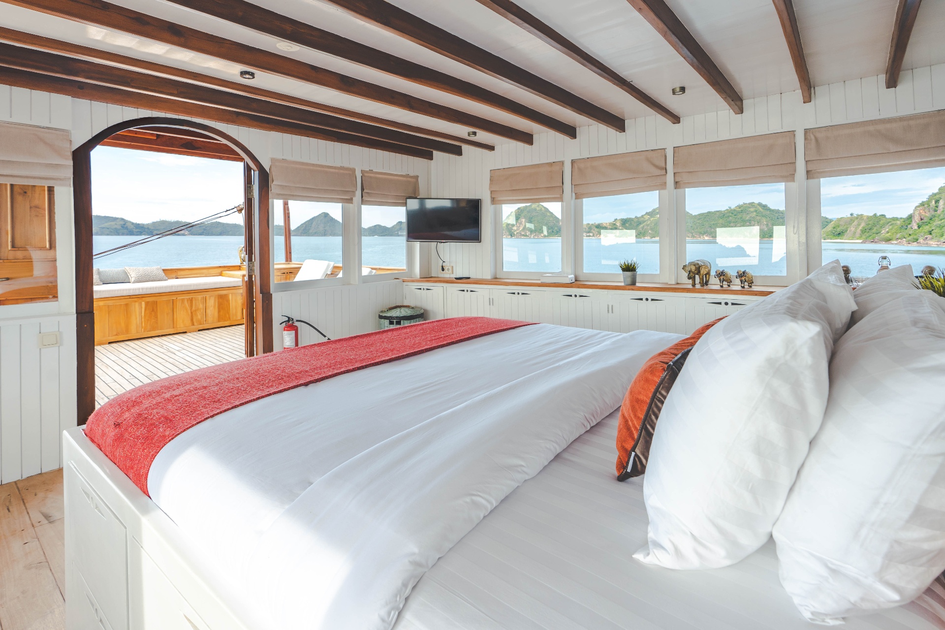 Mischief Komodo master suite with king bed, wooden beams, wall-mounted TV and arched doorway opening onto a private terrace
