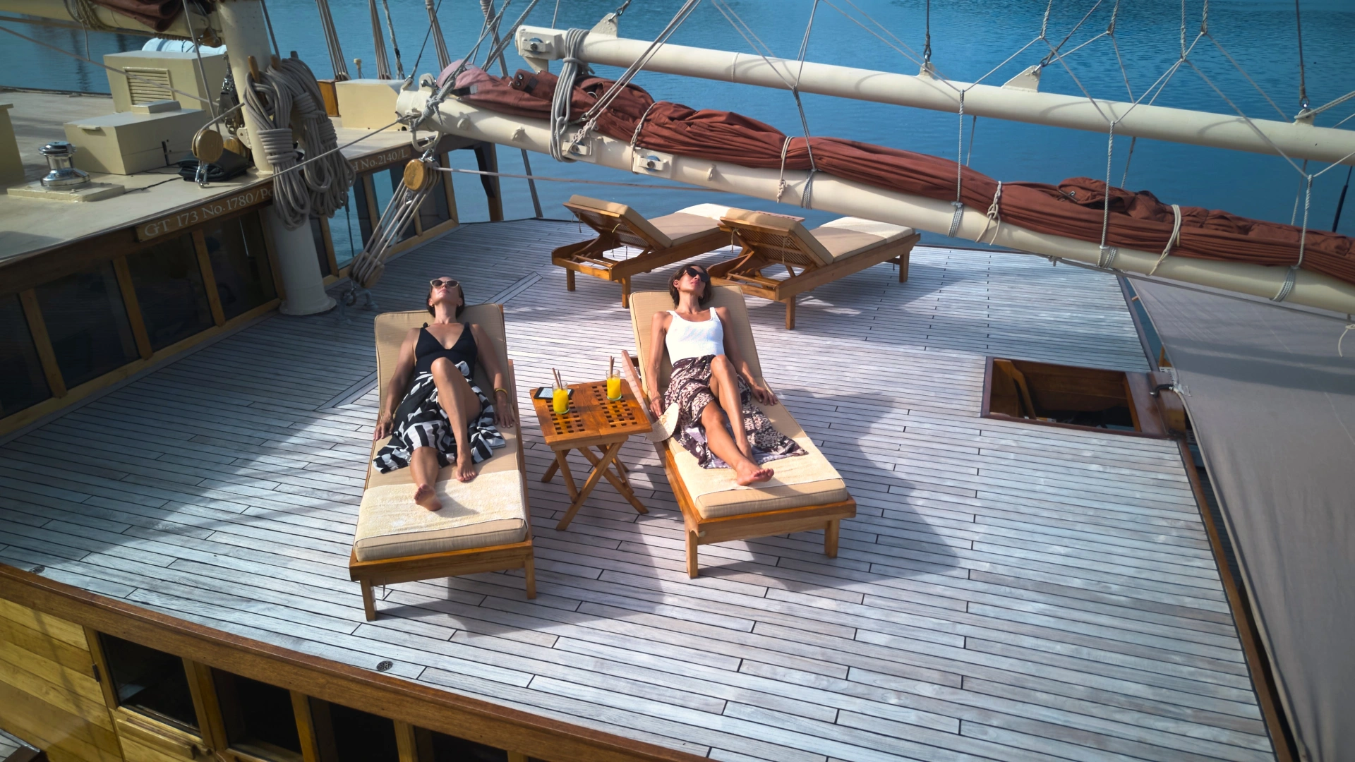 Two guests sunbathing on teak sundeck loungers aboard Si Datu Bua with fresh juices on a side table
