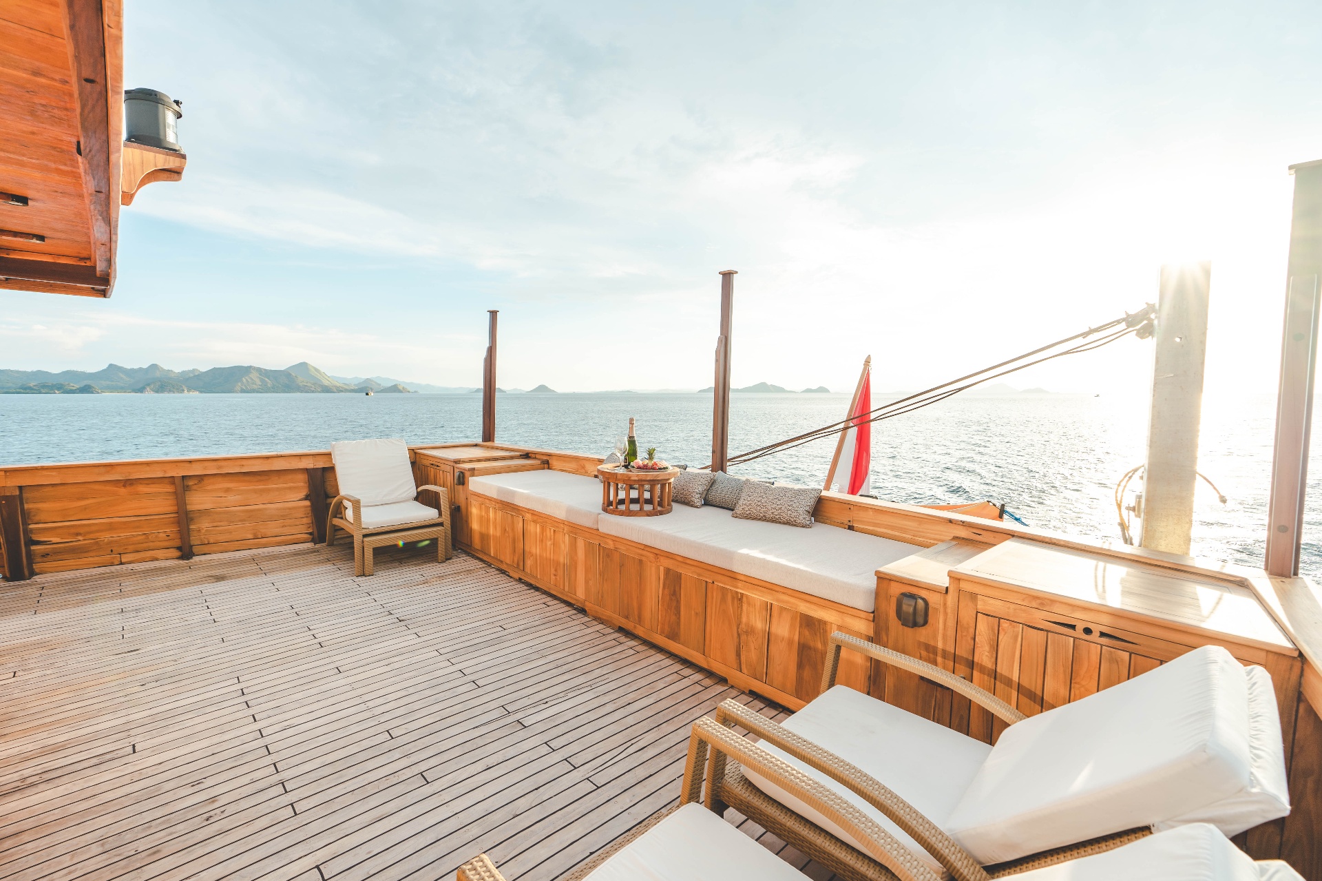 Mischief bow deck with cushioned daybed, rattan sun loungers and teak decking bathed in afternoon light