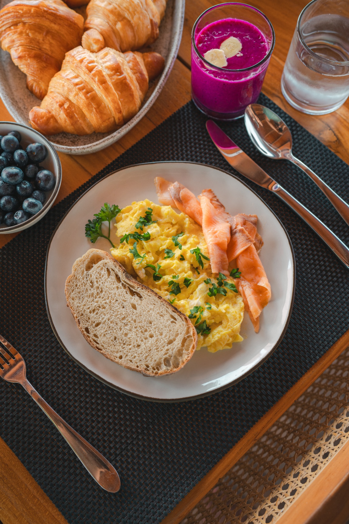 Scrambled eggs with smoked salmon and sourdough alongside croissants and dragon fruit smoothie on Mischief